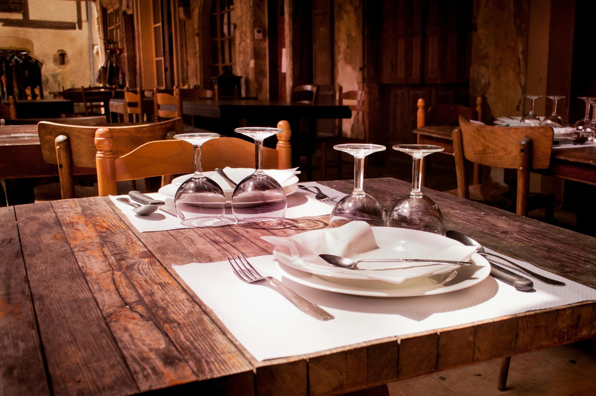 Rustic restaurant table set with white plates, folded napkins, and wine glasses in a warm wood interior
