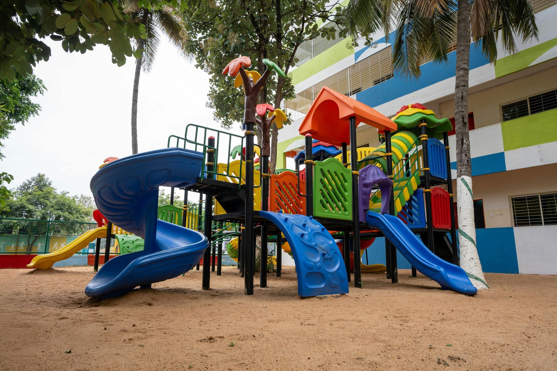 Colorful playground with slides, climbing structures, and trees on a sandy surface
