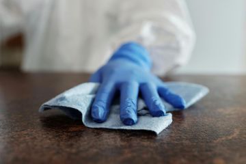 Gloved hand wiping a dark table with a blue cloth