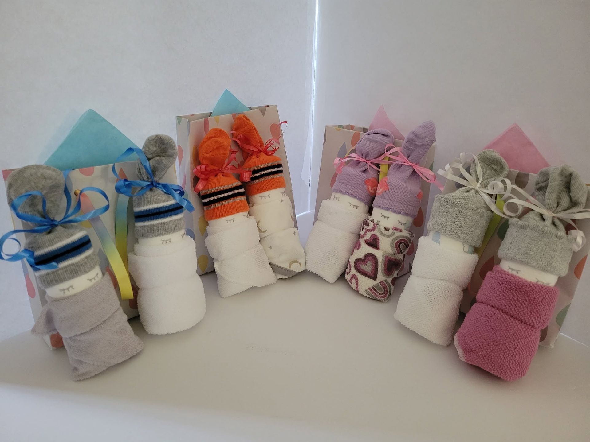 Six small rolled fabric bundles tied with ribbon in pastel colors on a white surface
