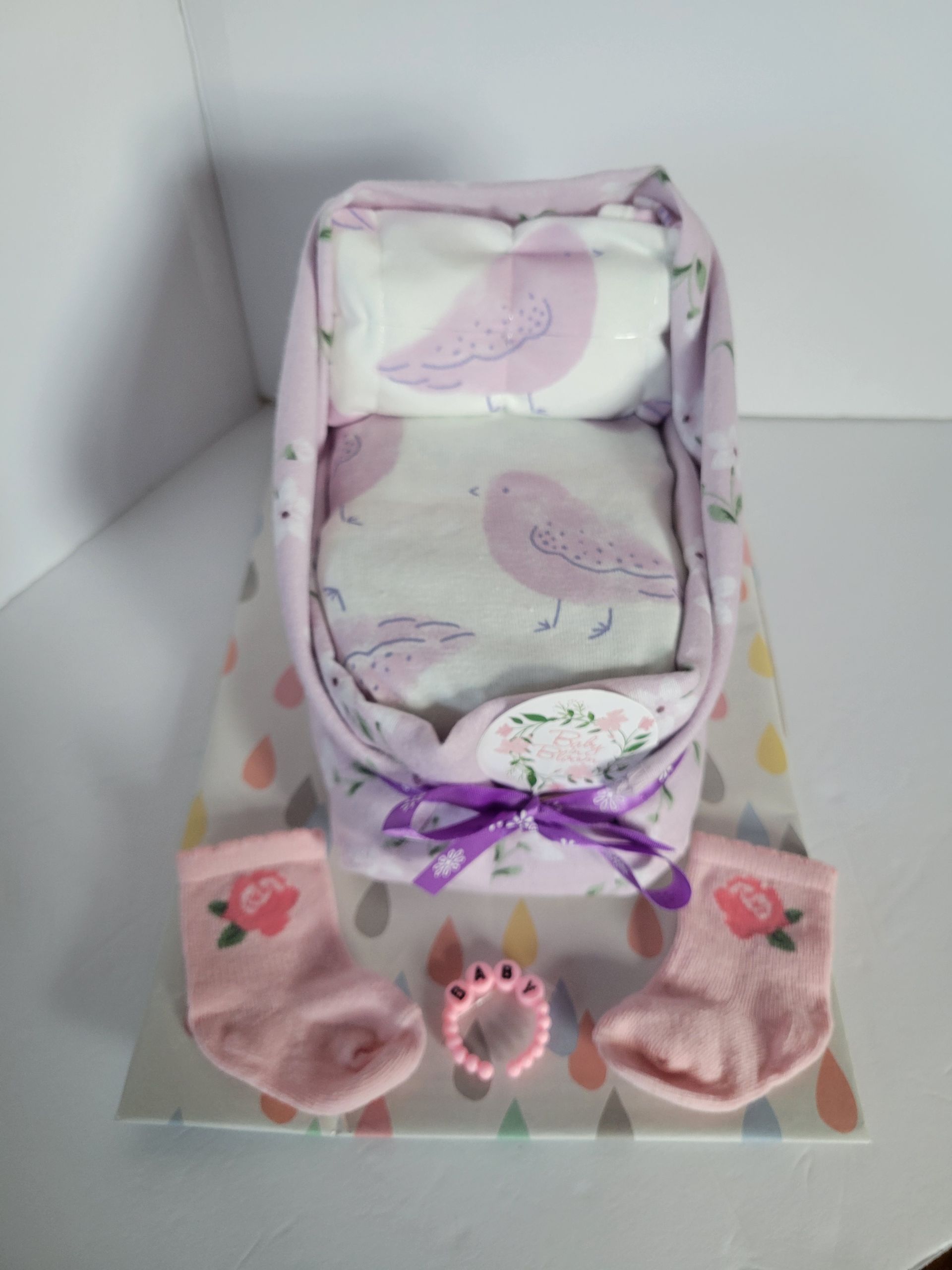Small purple-and-pink gift basket with floral tissue paper and ribbon, on a white surface.