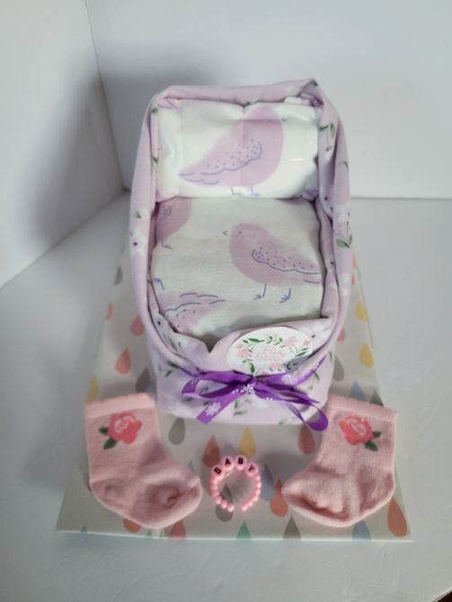 Purple gift box with baby items and pink socks on a white shelf