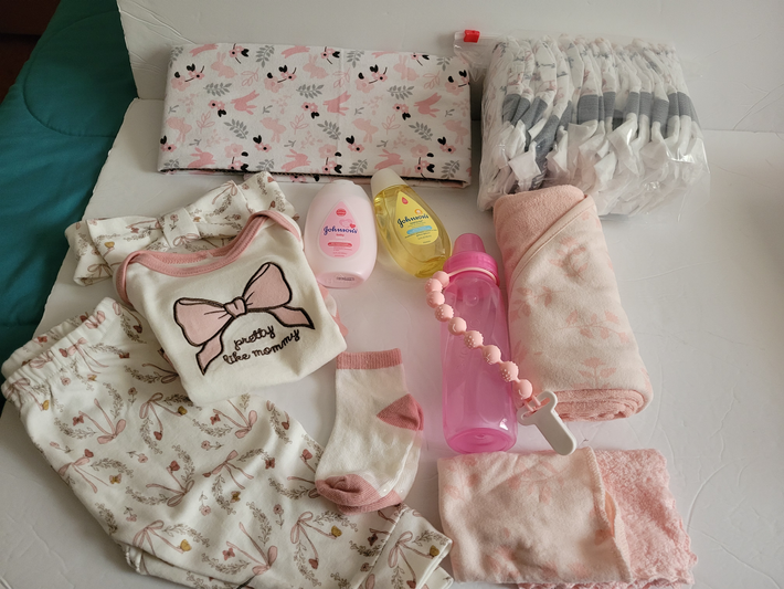 Assorted pink toiletry and makeup items arranged on a bed, including bags, lotion, and a water bottle