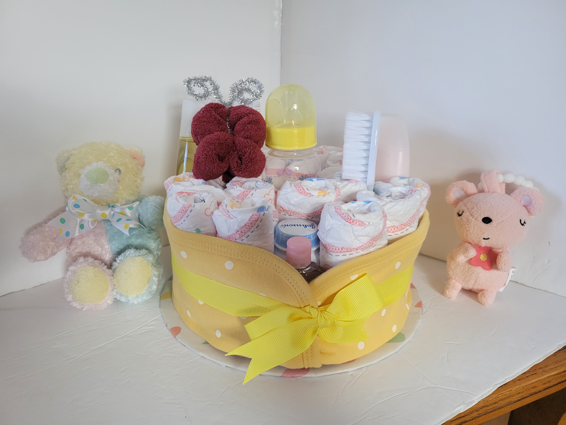 Pastel yellow baby gift basket with plush toys, cupcakes, and ribbon on a white table