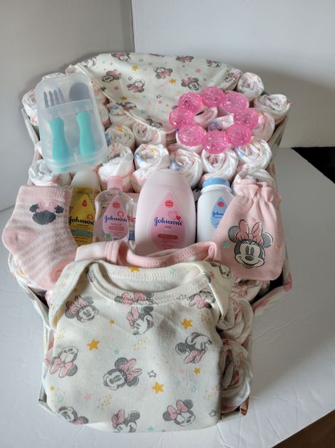 Baby gift basket with floral blankets, pink items, bottles, and a stuffed toy on a white surface