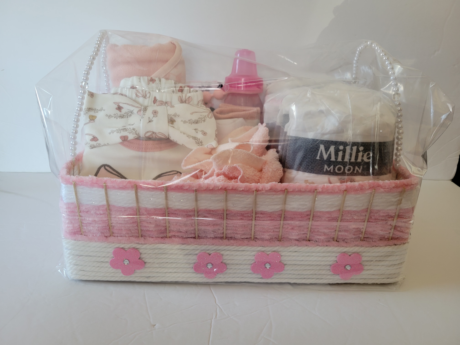 Pink gift basket with baby items, including a bottle, blanket, and accessories in clear cellophane.