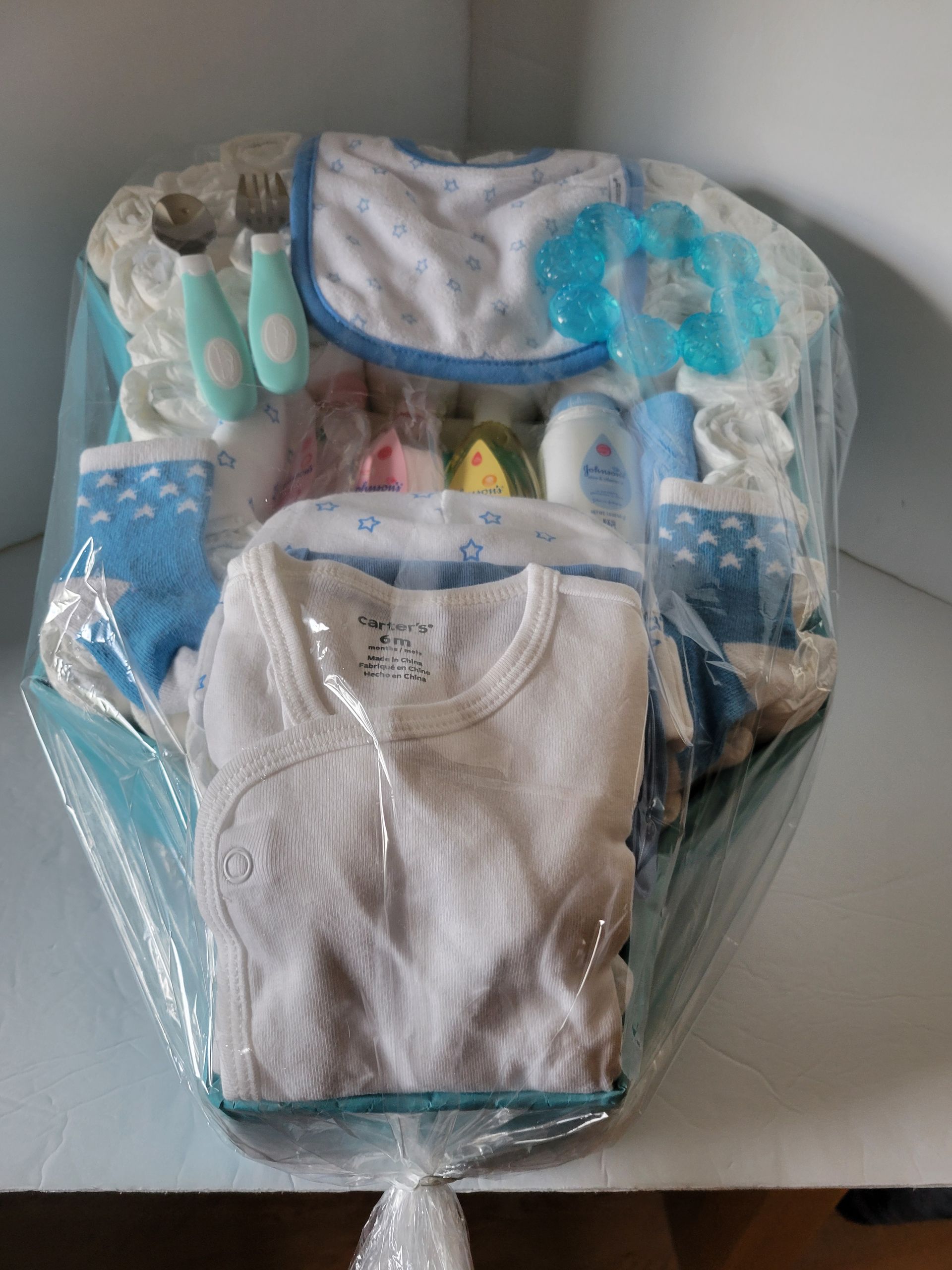 White baby onesies in a decorated blue gift basket with ribbon and tissue paper
