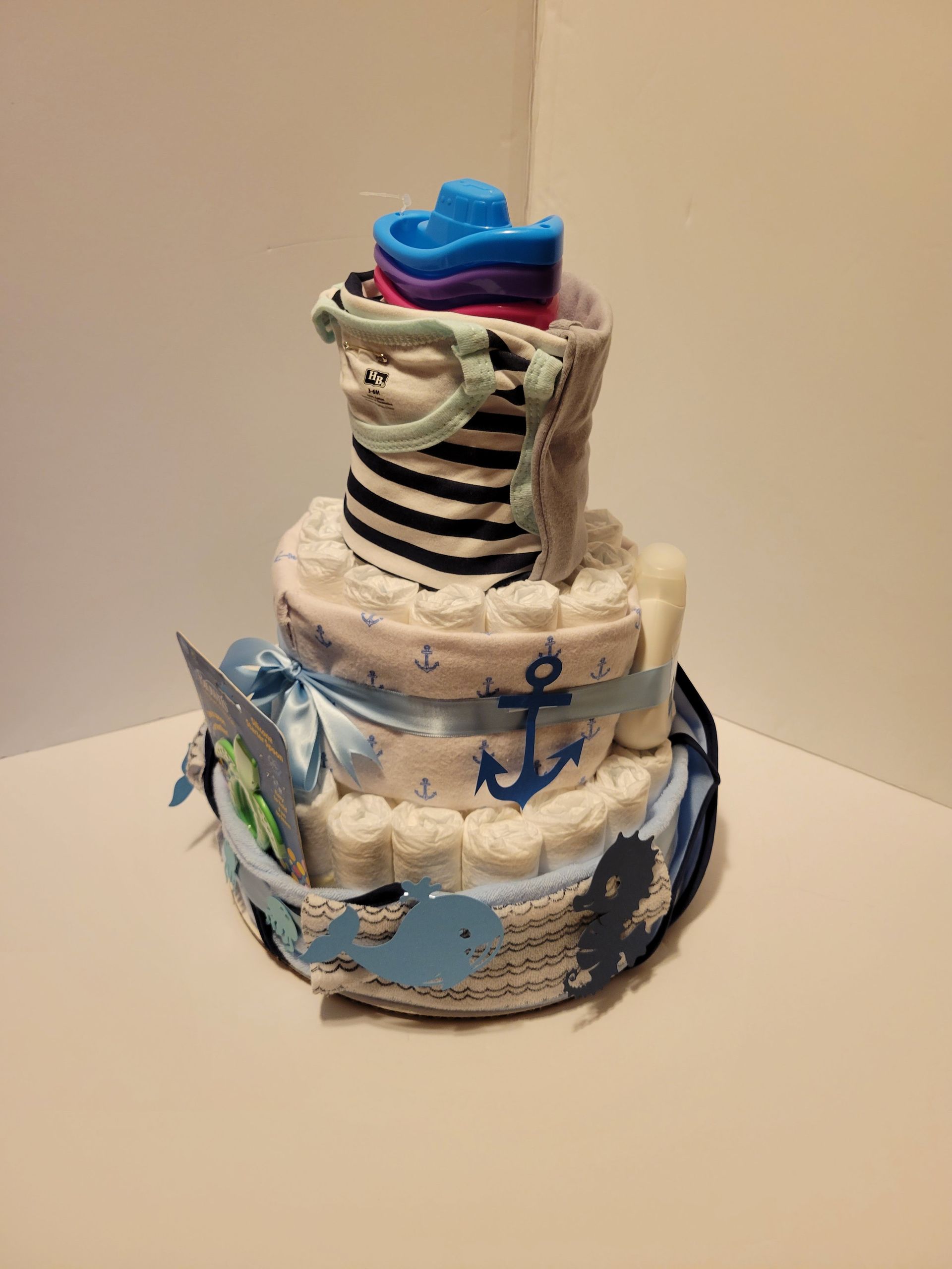 Wrapped multi-tier cake with blue ribbon and baby-themed decorations on a white table