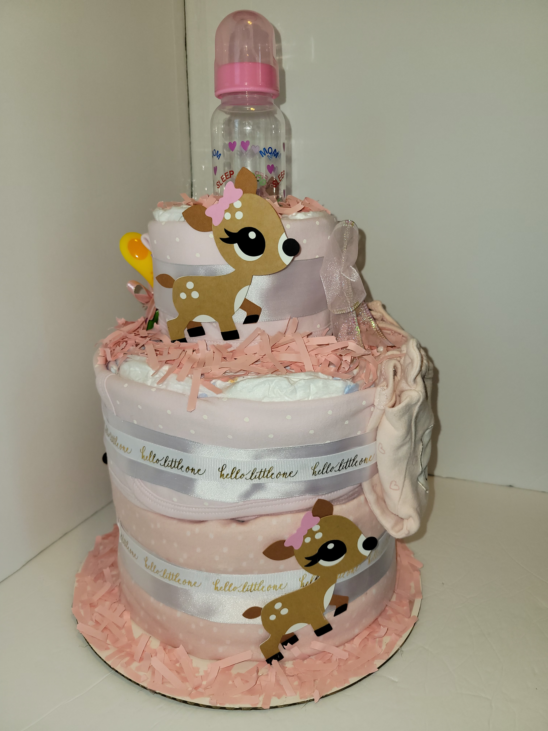 Pink-decorated baby bottle gift wrapped with white and pink ribbons and small fawn ornaments
