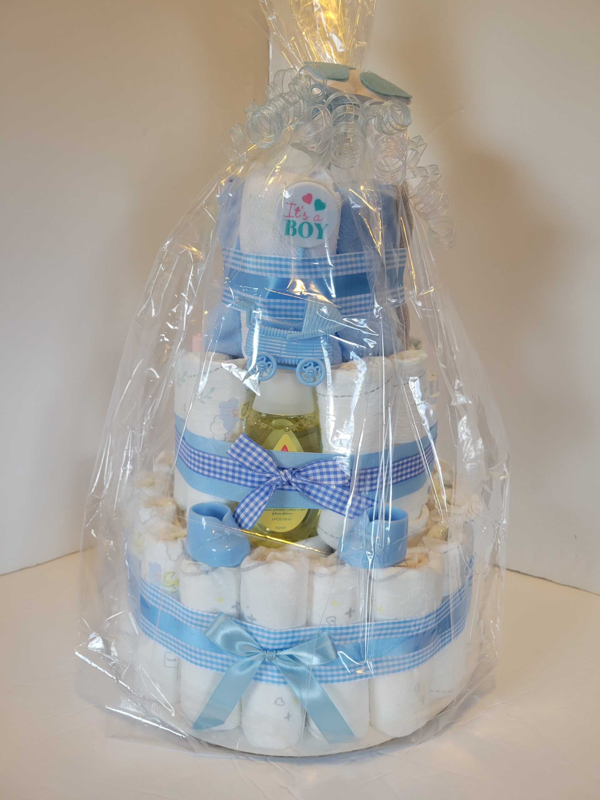 Blue and white diaper cake with teddy bear topper and ribbon bows on a stand