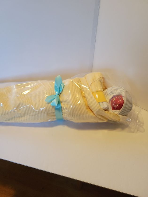 Wrapped yellow object tied with blue ribbon on a white surface, with a red tip at one end