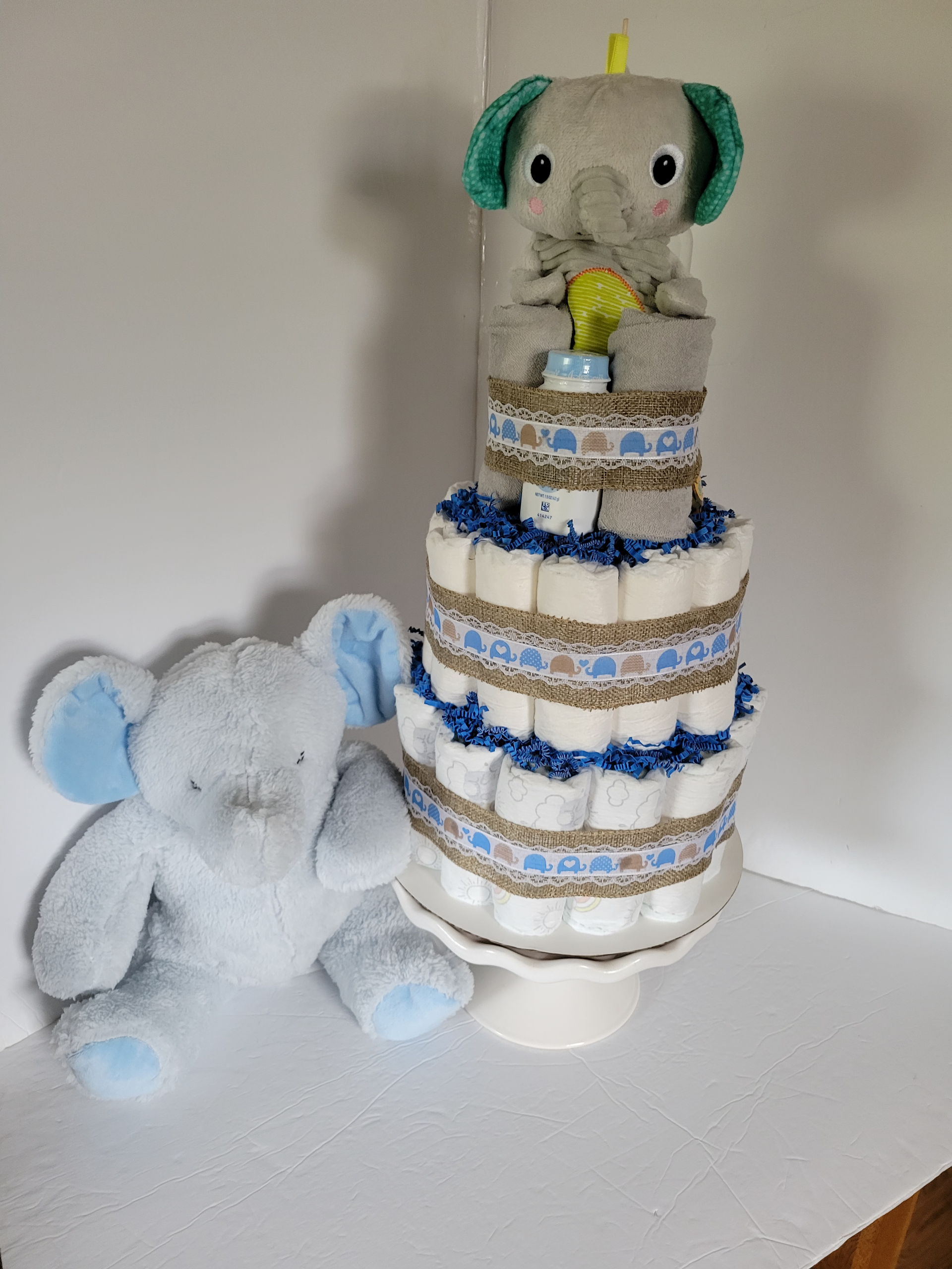 Stuffed animals on a white cake stand: a grey elephant atop a blue-and-white diaper cake