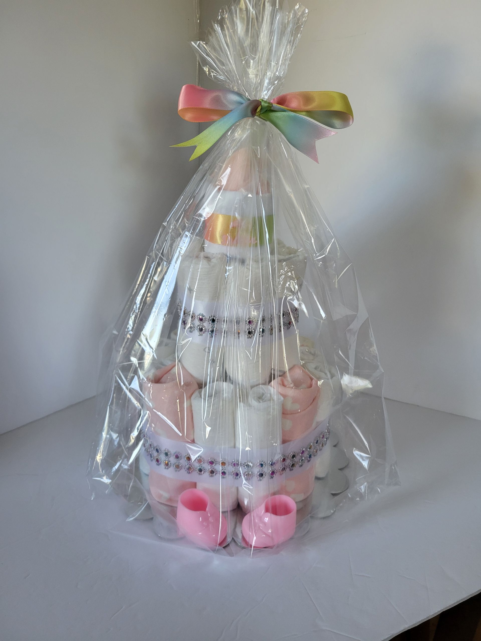 Tiered diaper cake with pastel pink and white rolled diapers, decorated with ribbon and topped with a baby bootie.
