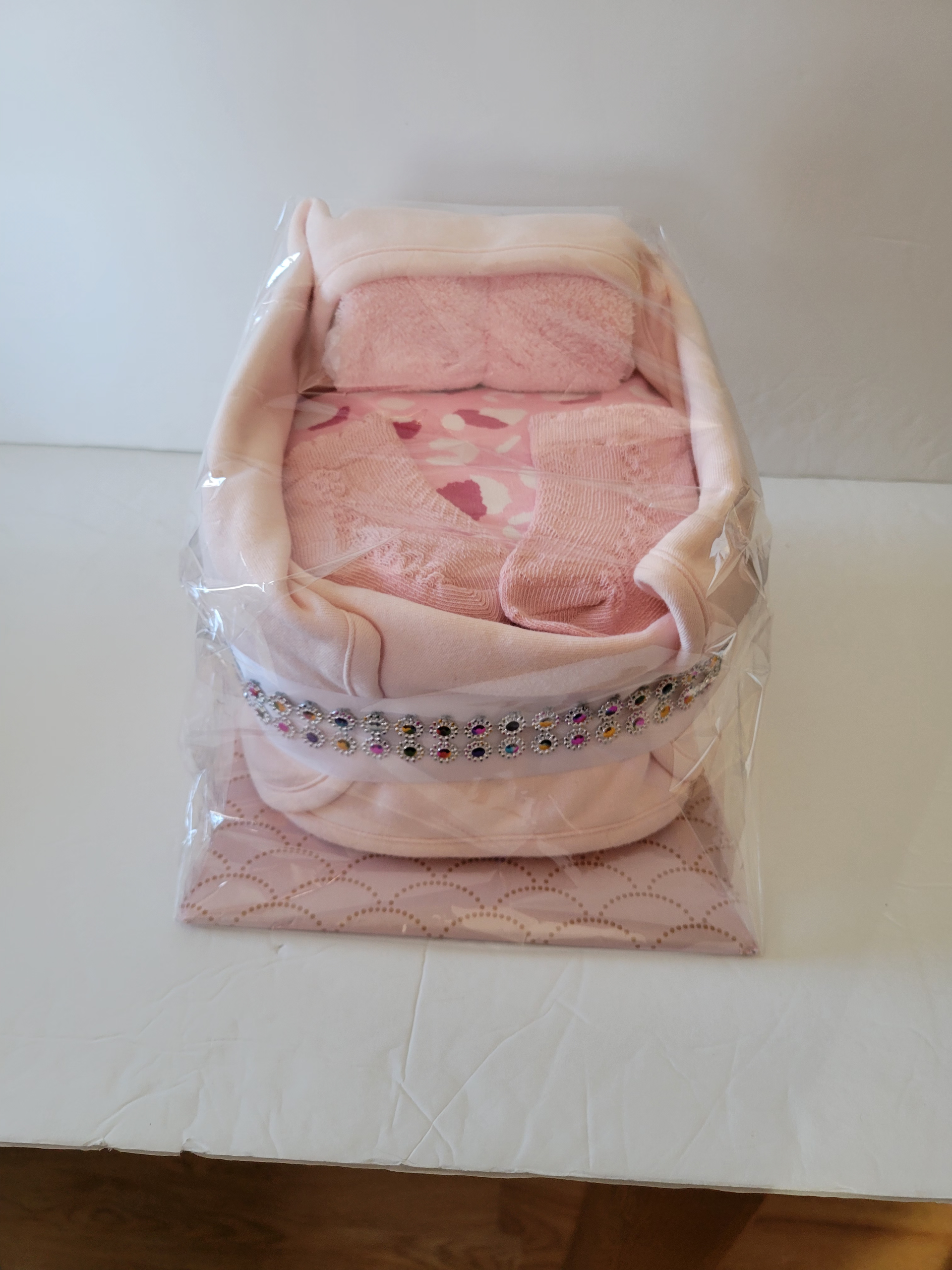 Pink baby blanket folded in a clear plastic gift basket on a white table