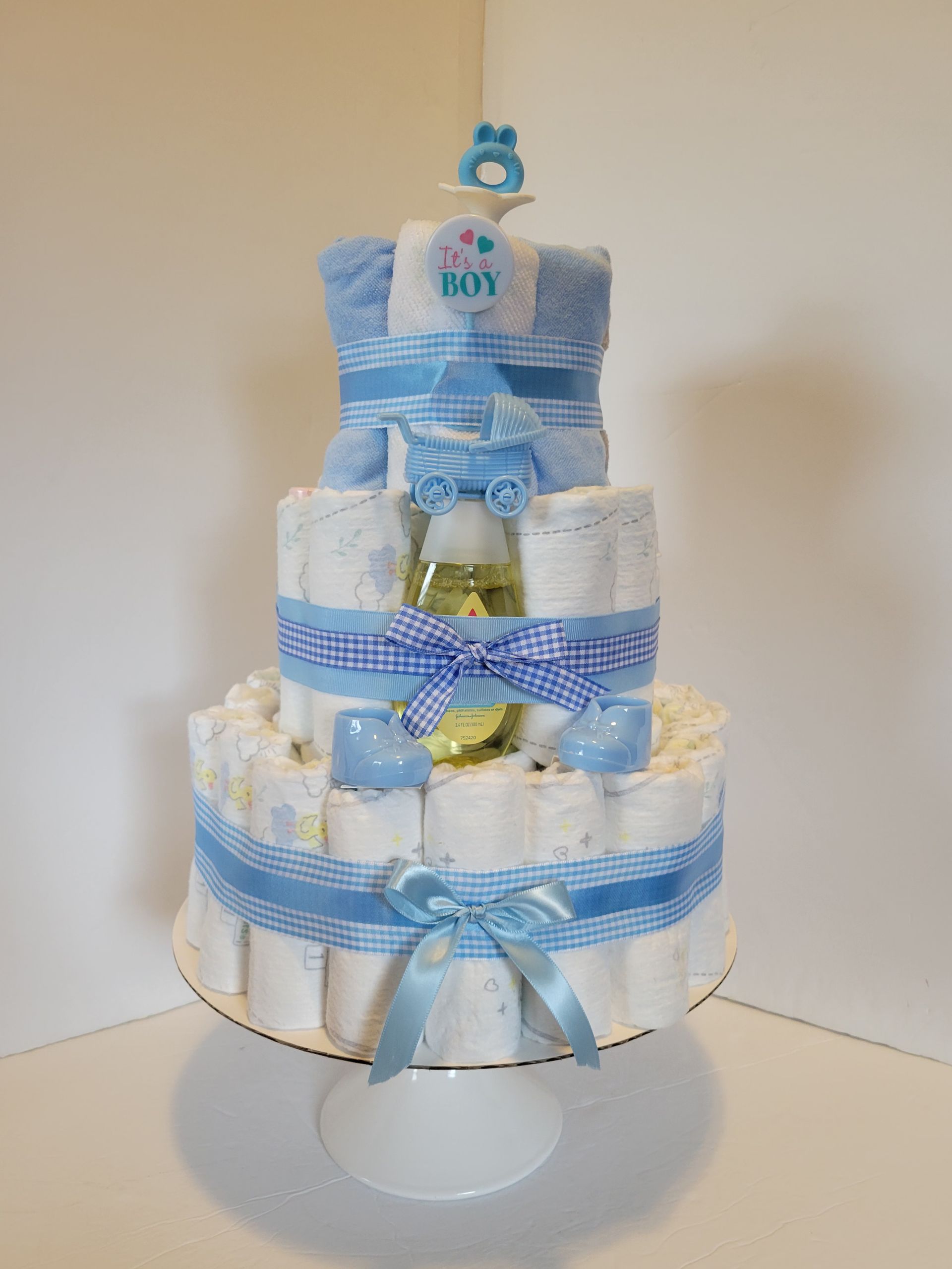 Blue and white diaper cake with teddy bear topper and ribbon bows on a stand
