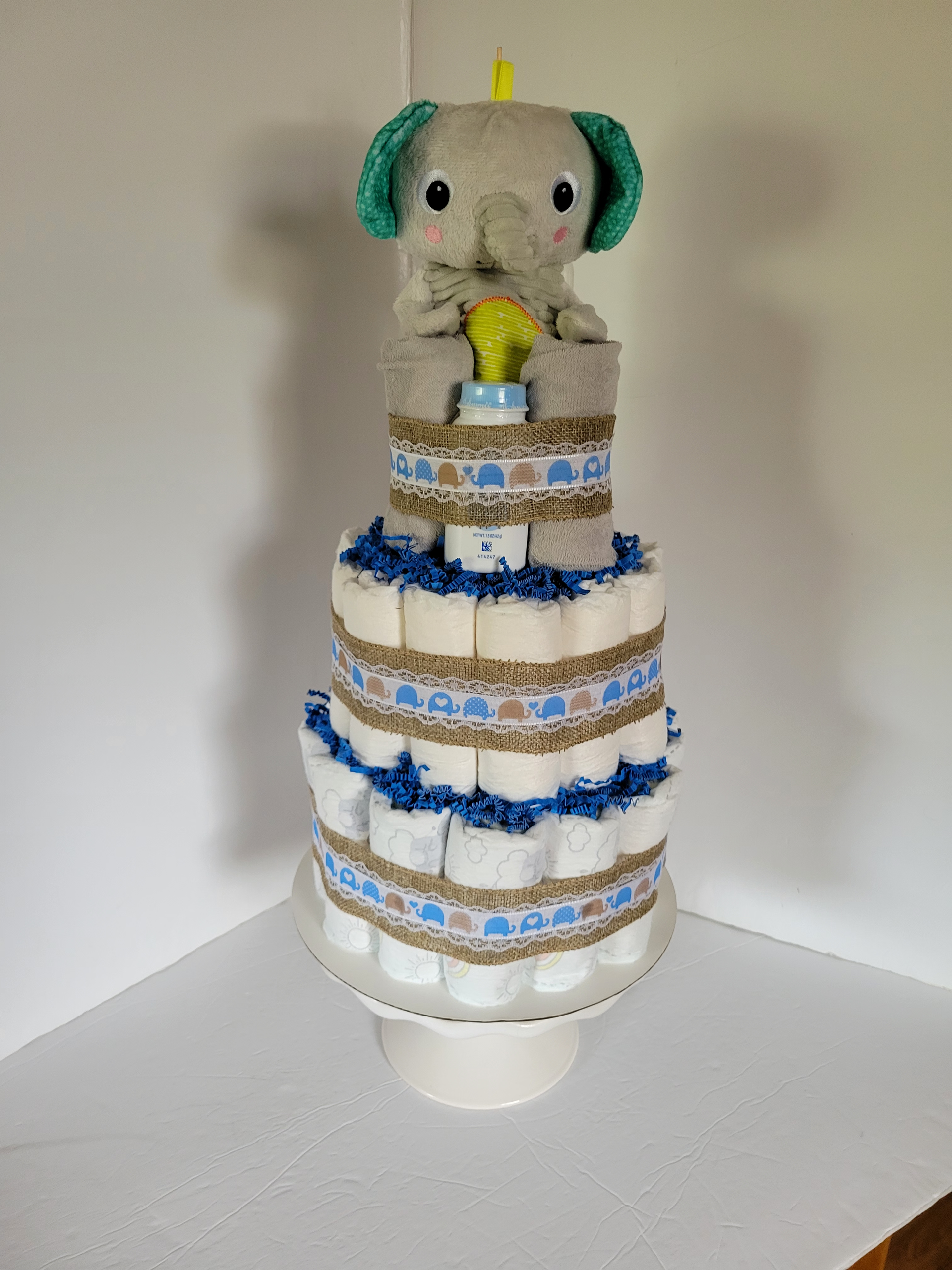 Stuffed animals on a white cake stand: a grey elephant atop a blue-and-white diaper cake