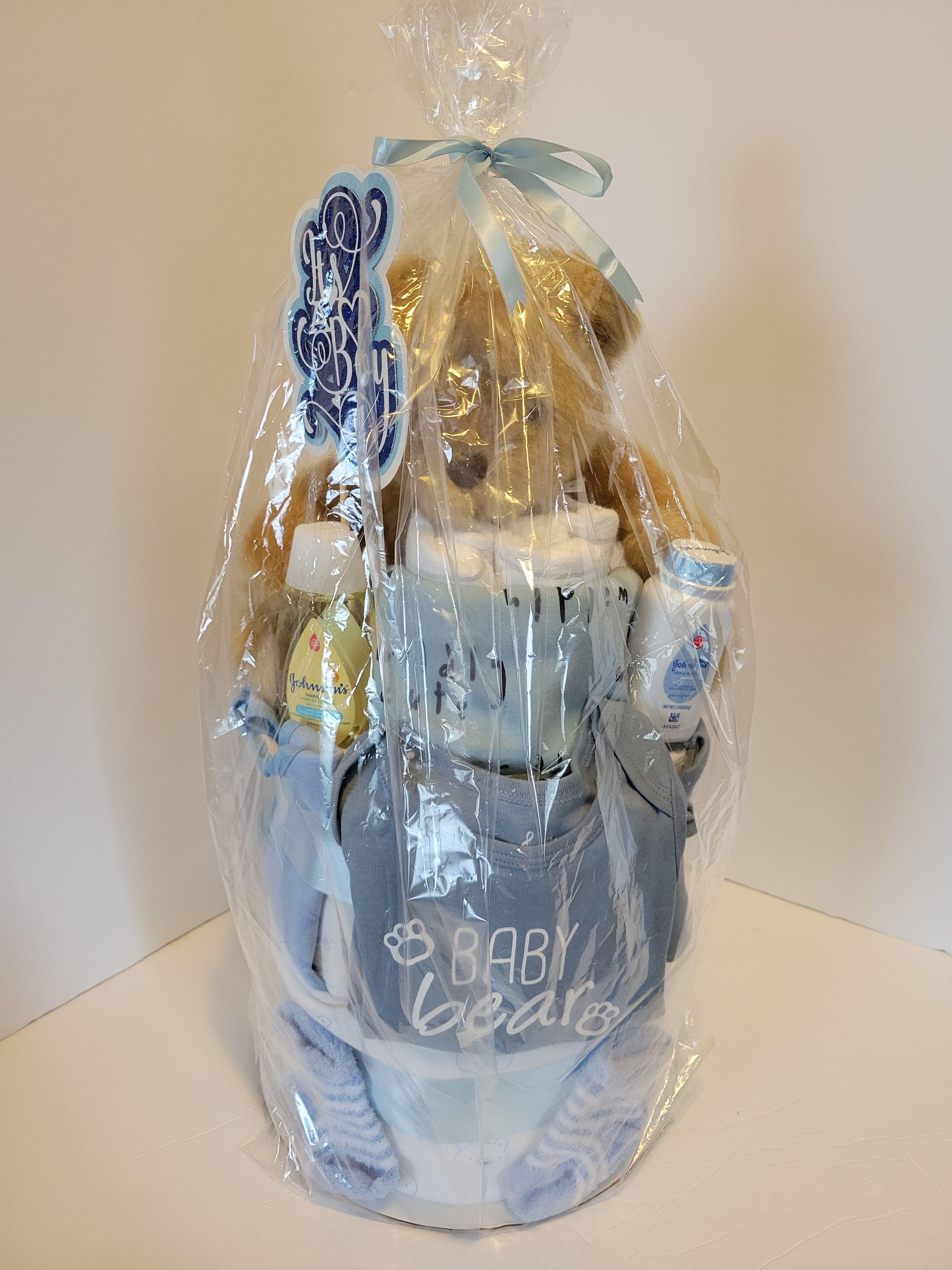 Teddy bear in a baby gift basket with a gray “Baby Bear” bib, cups, and blue booties