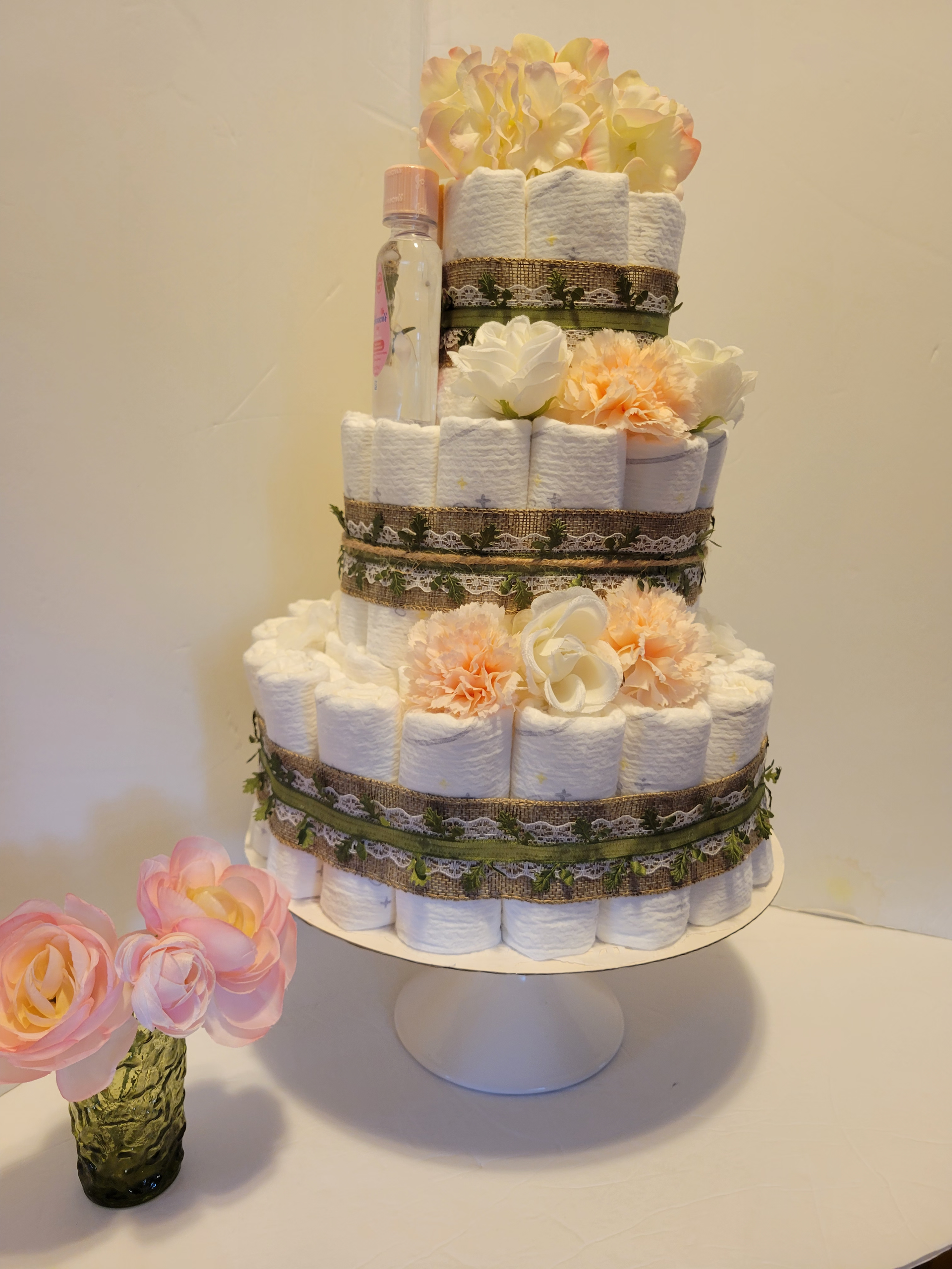 Two-tier white floral centerpiece with peach and pink flowers on a stand, plus small flowers in a vase nearby