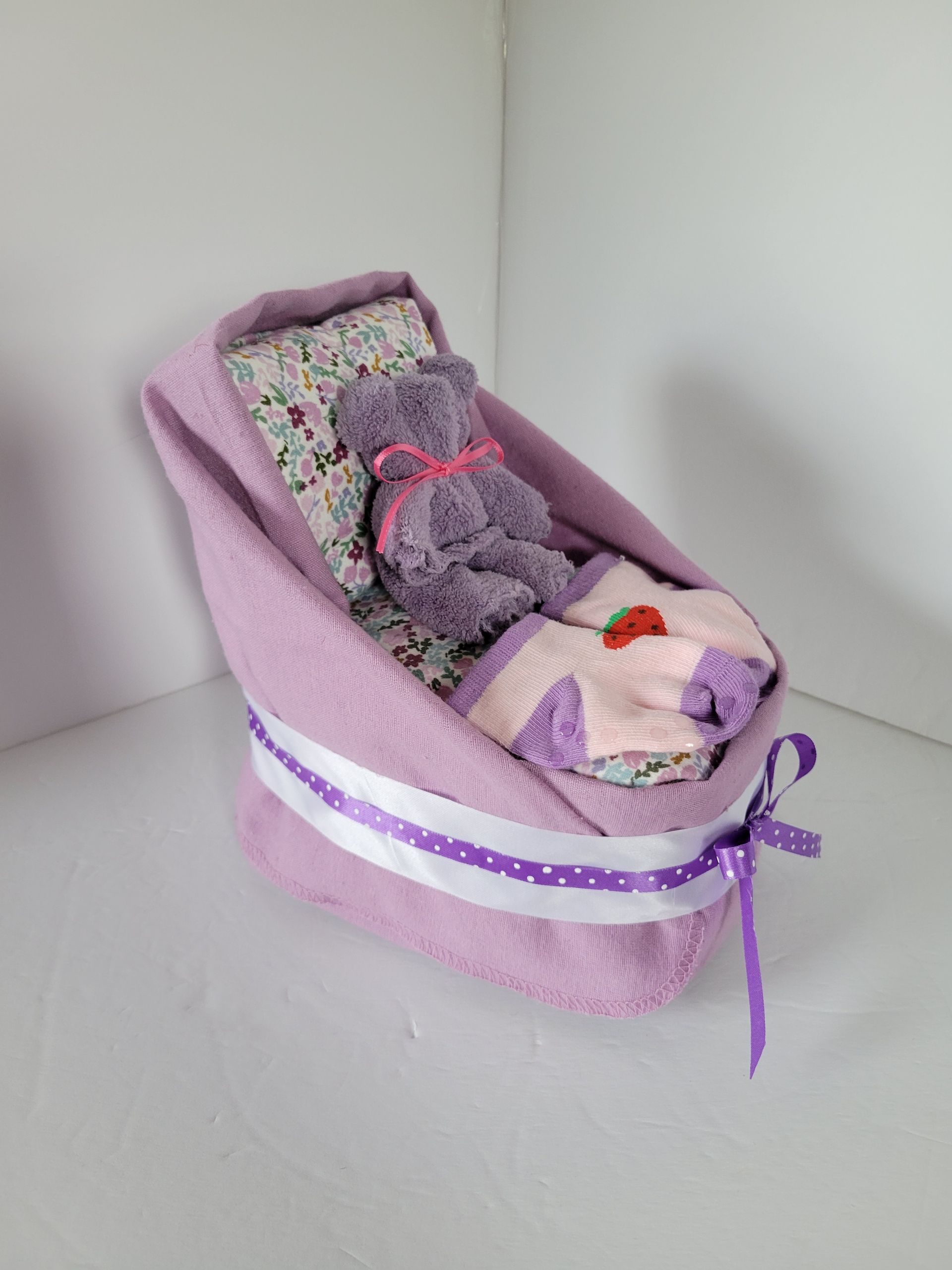 Purple fabric doll chair with floral cushion and ribbon bows on a white surface