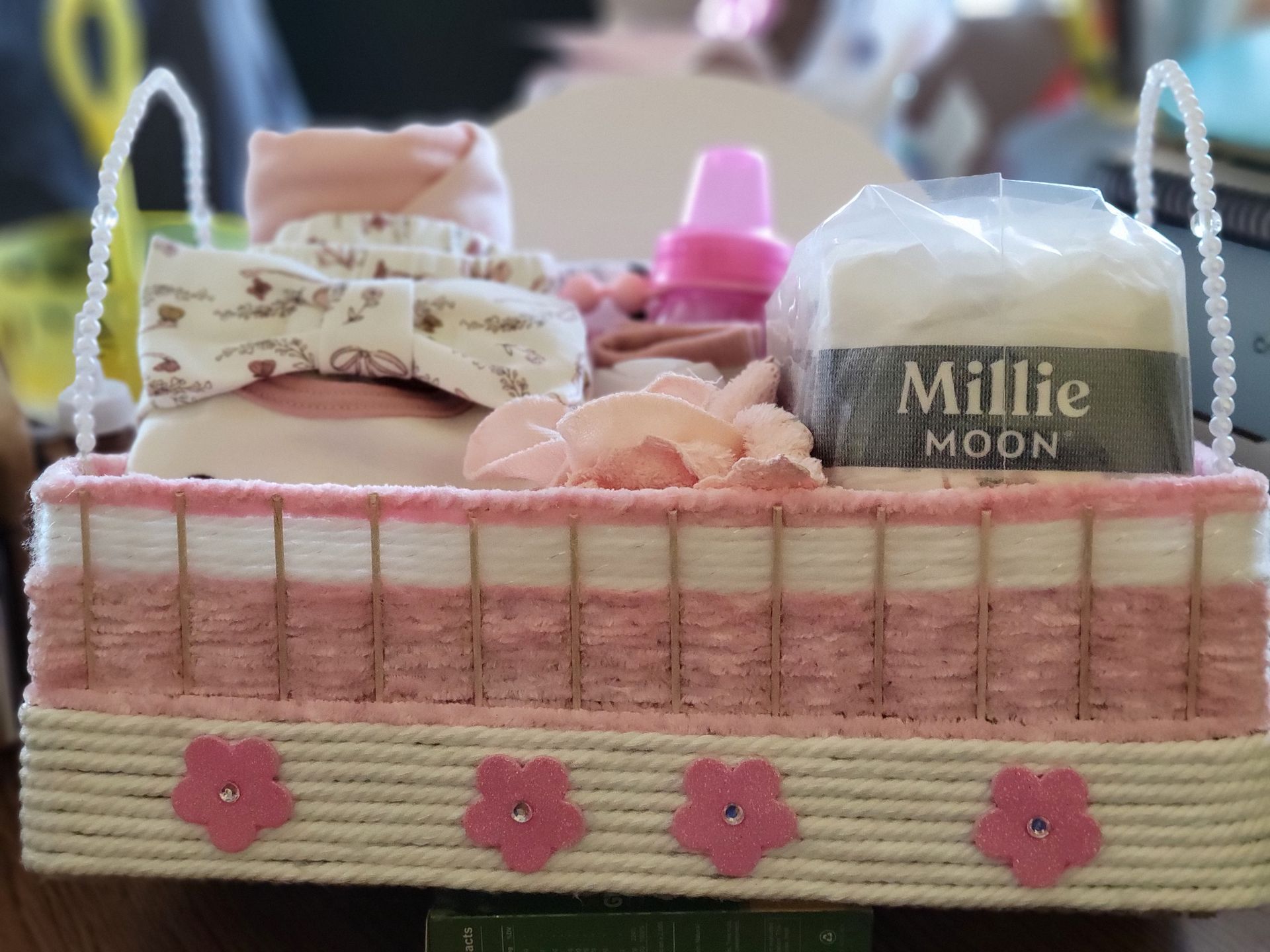 Assorted pink floral and pastel personal items laid out on a bed, including pouches, bottles, and a bottle carrier