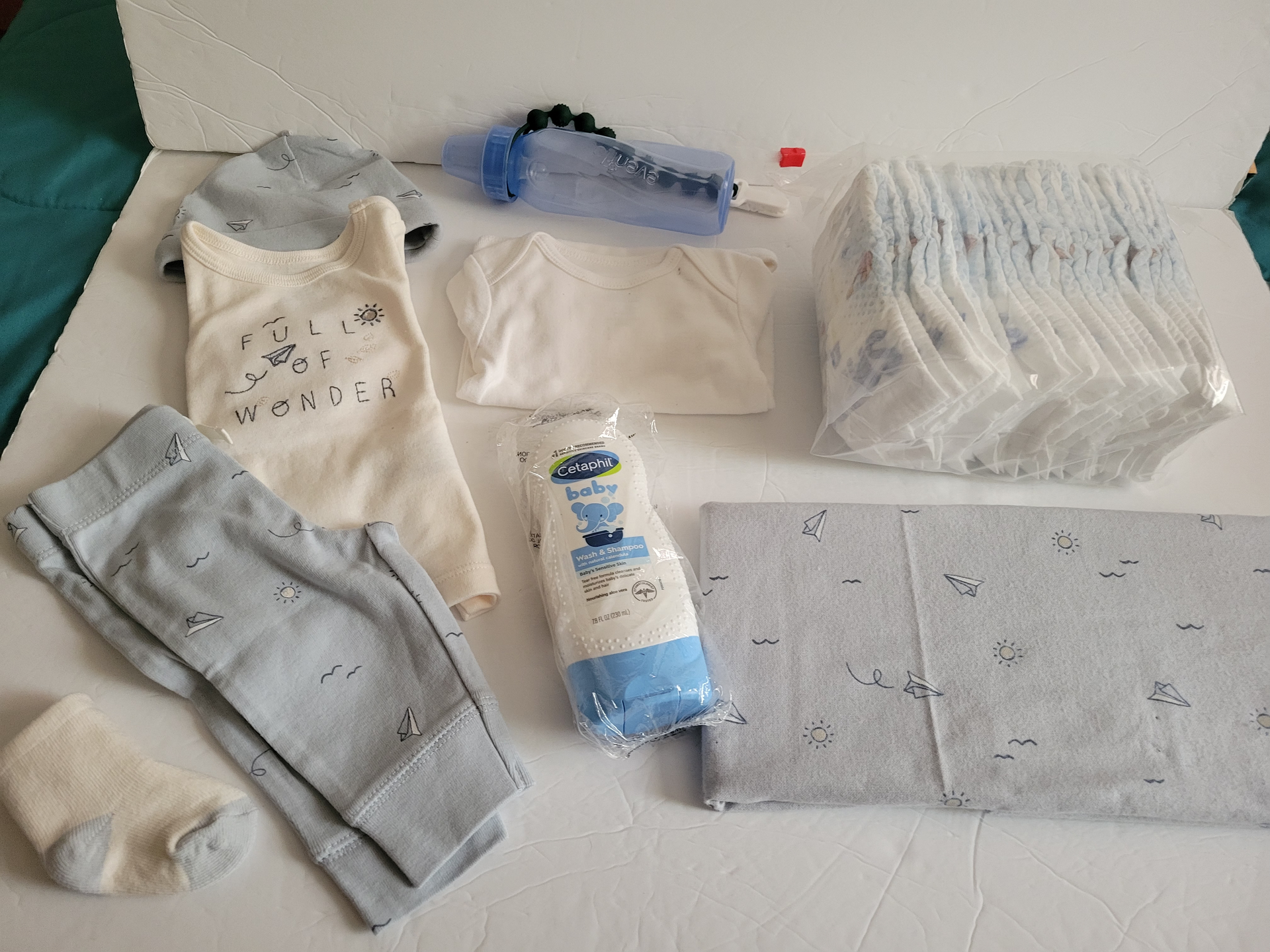 Assorted baby clothes, diapers, wipes, and bottles laid out on a bed or changing surface.