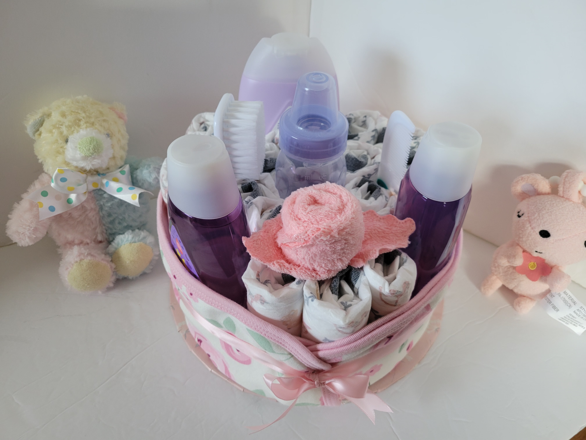 Gift basket with pink toiletries and a teddy bear on a white shelf, flanked by small stuffed animals