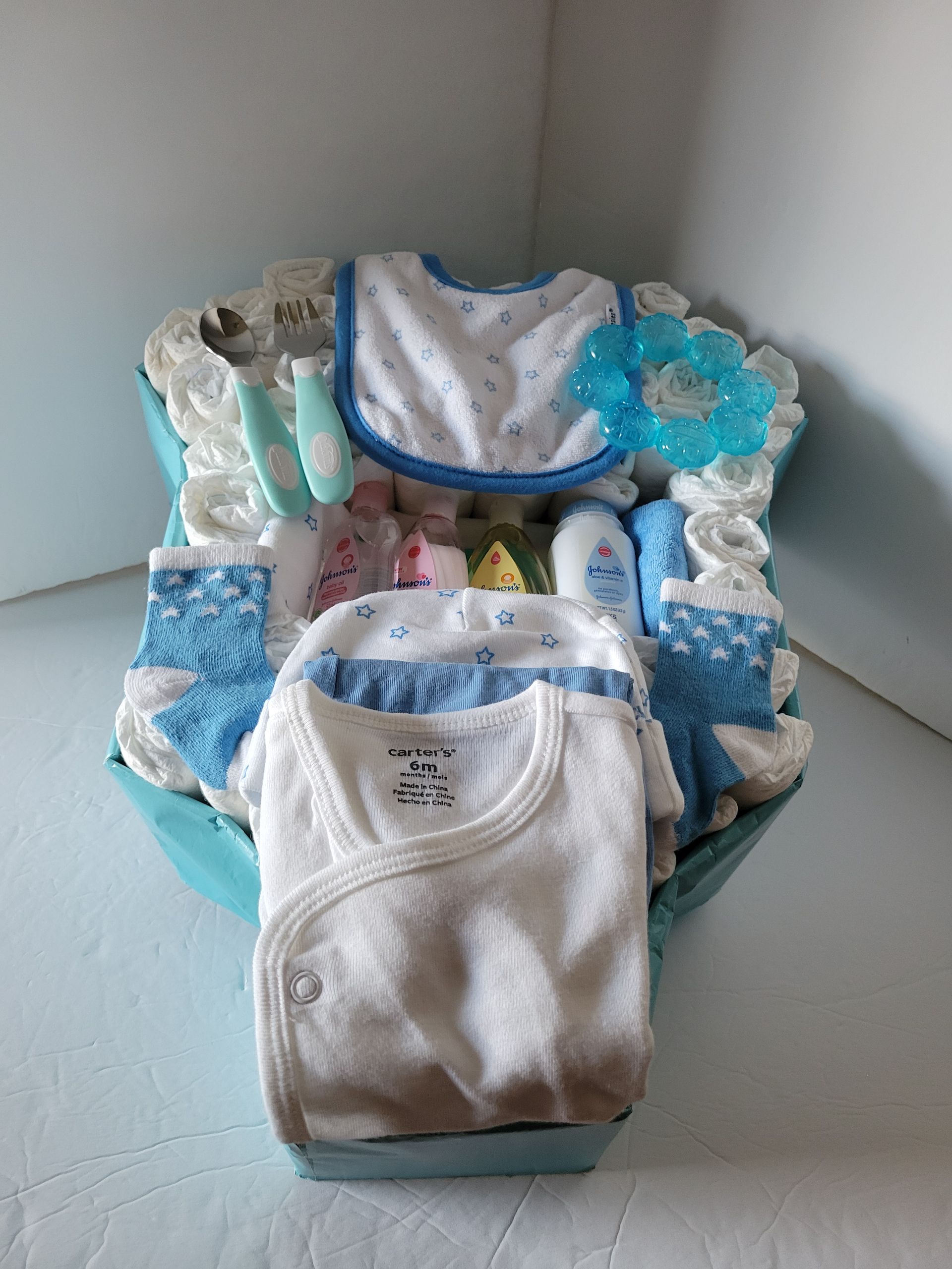 White baby onesies in a decorated blue gift basket with ribbon and tissue paper