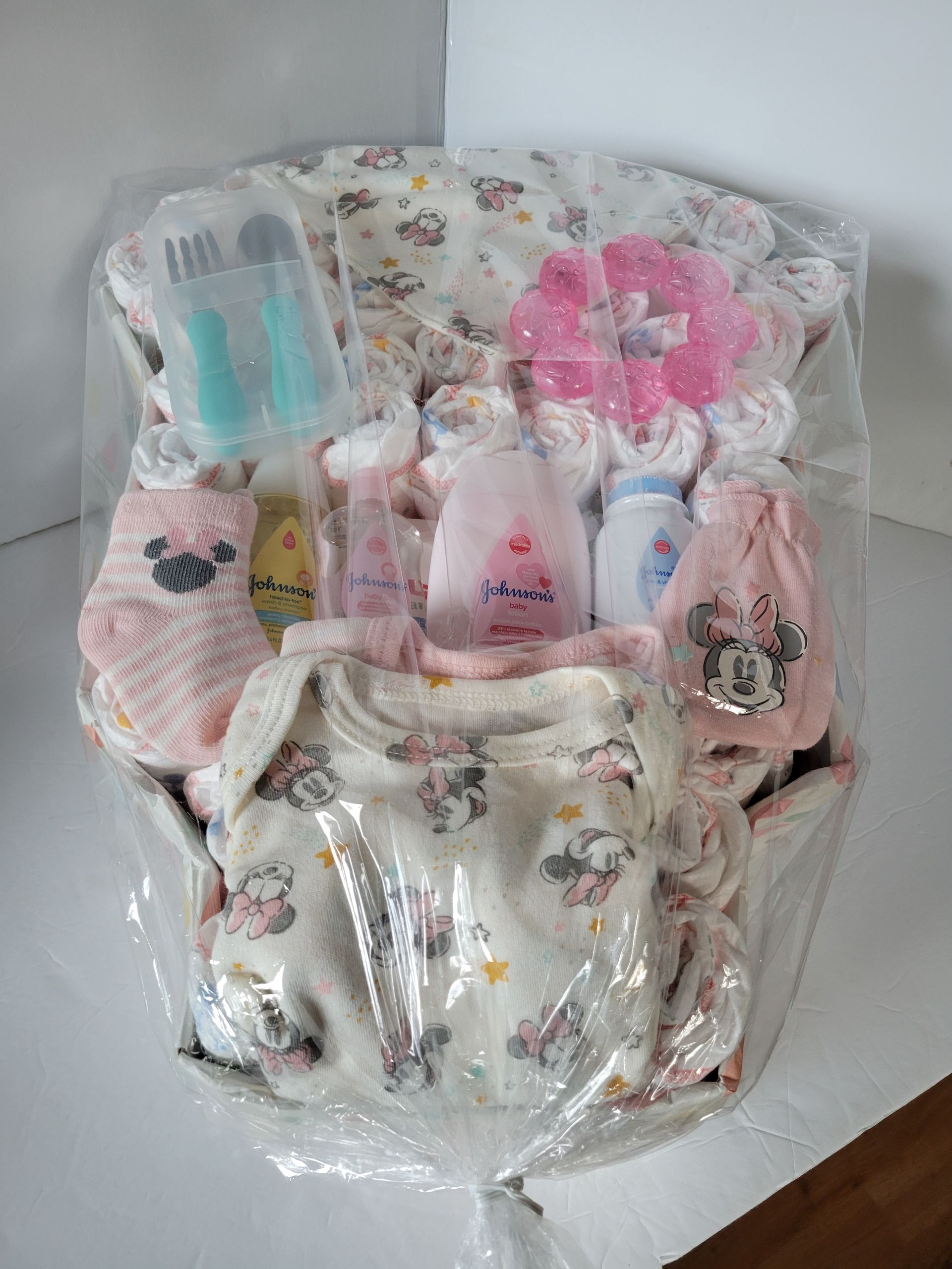 Assorted baby items in clear plastic packaging, including bottles, socks, clothes, and a pink flower accessory