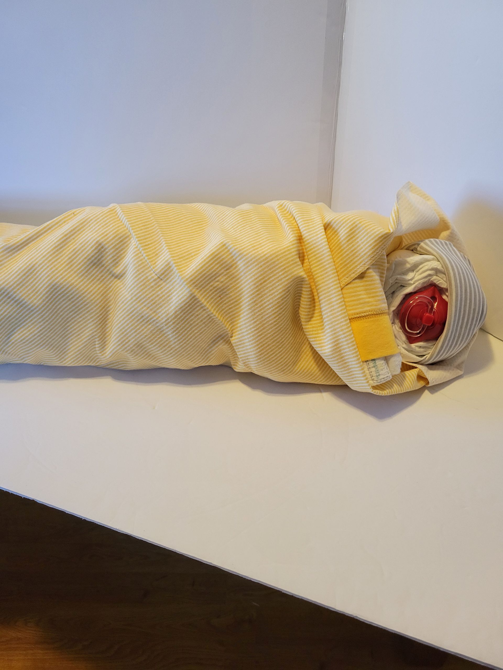 Wrapped doll or figurine in yellow fabric on a table, with a red face and hat visible.