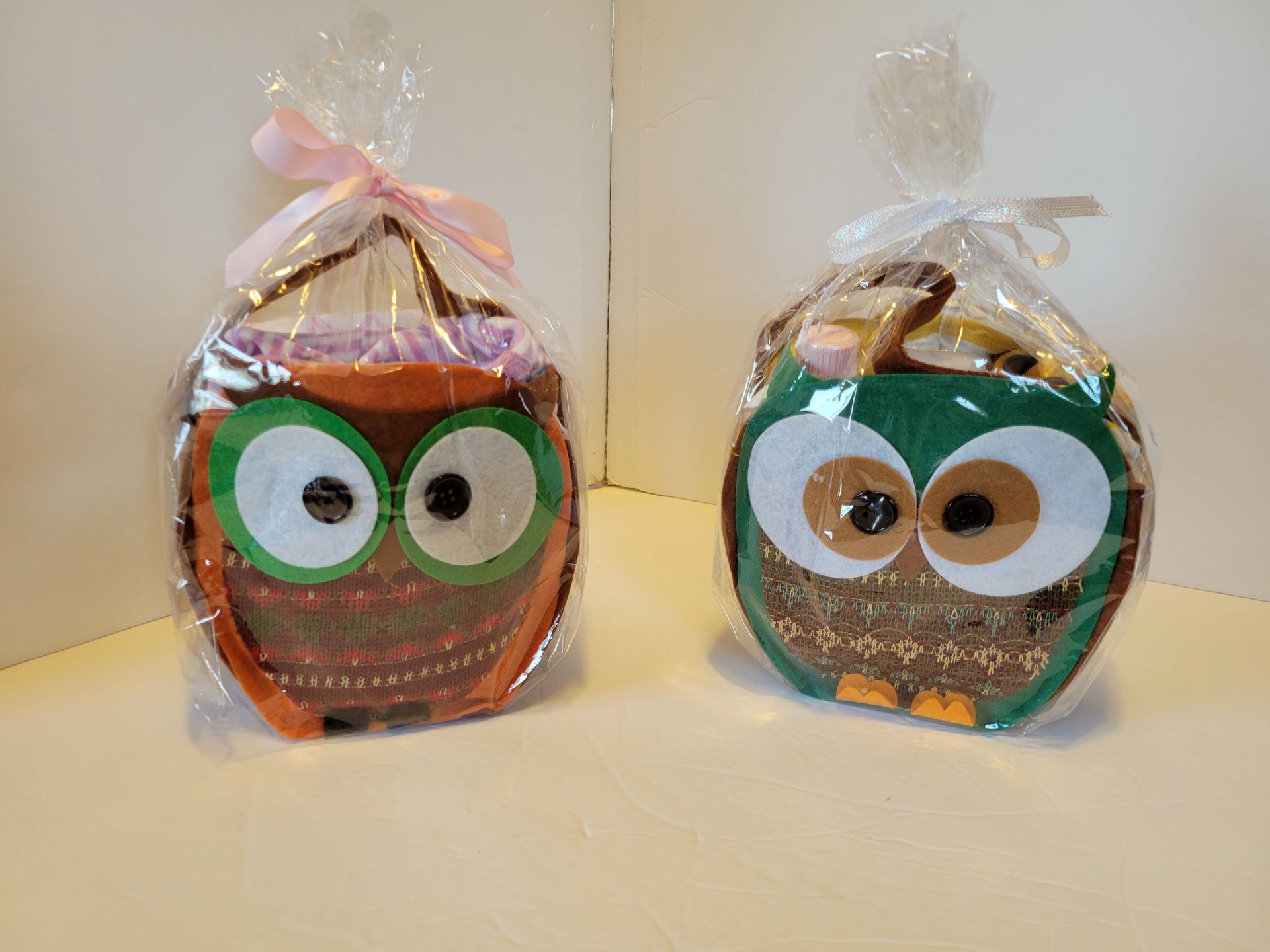Two wrapped gift bags with owl faces, one orange with pink ribbon and one green with clear ribbon.