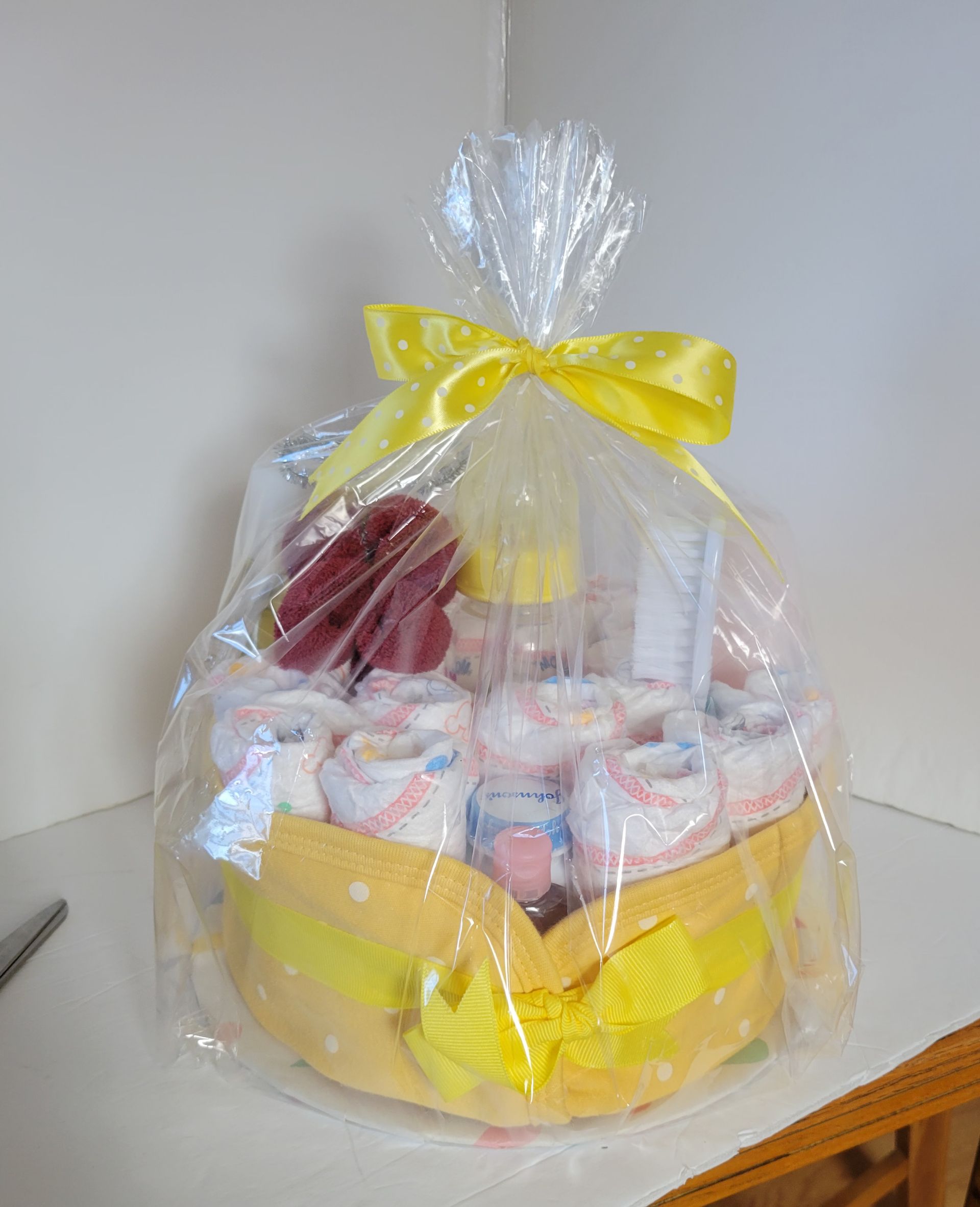 Pastel yellow baby gift basket with plush toys, cupcakes, and ribbon on a white table