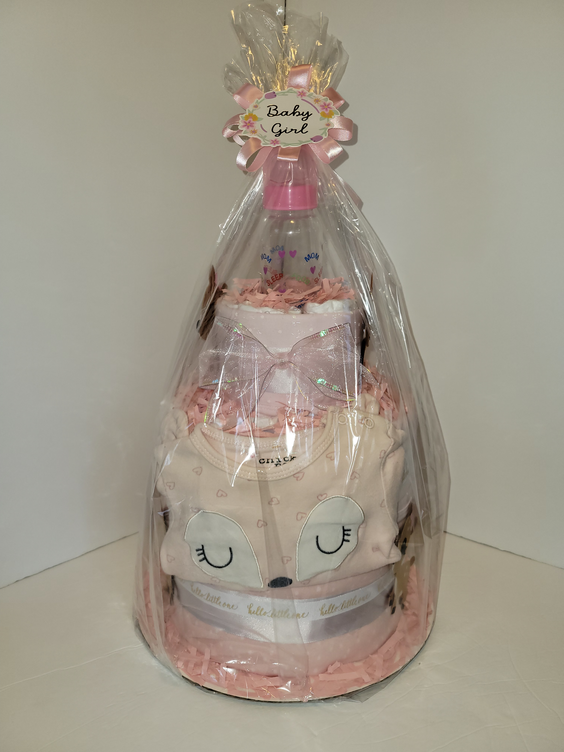 Pink-decorated baby bottle gift wrapped with white and pink ribbons and small fawn ornaments