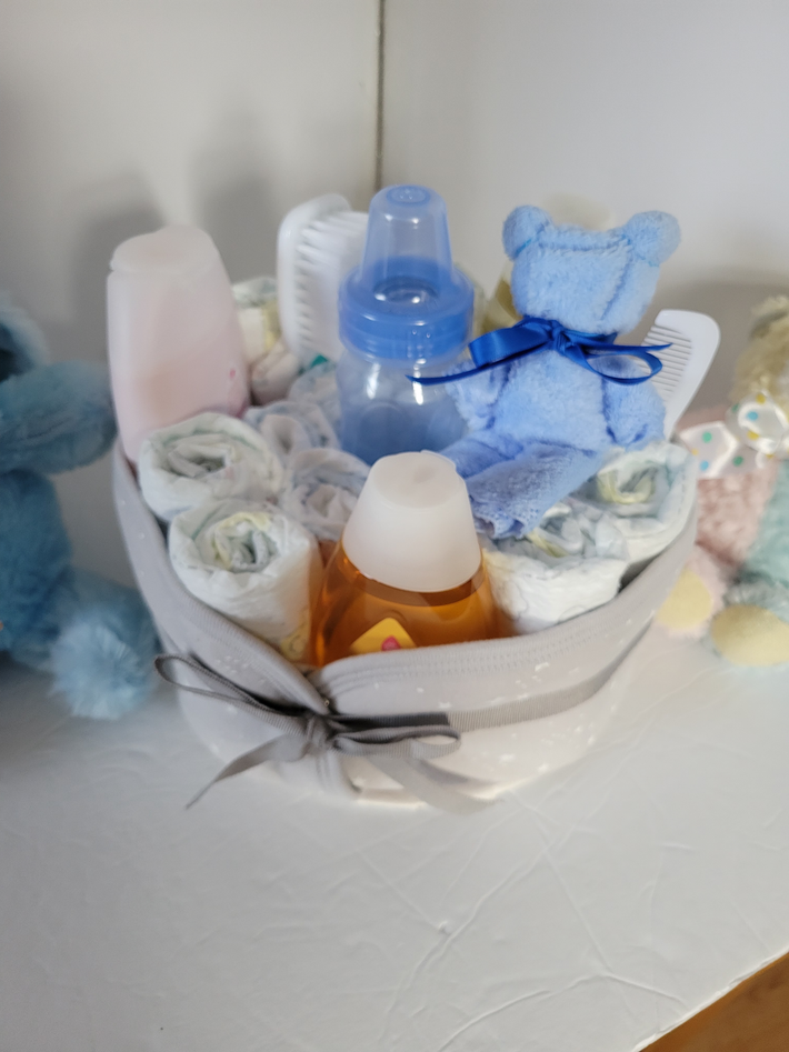 A baby gift basket with blue and white items, bottles, and soft blankets tied with a ribbon.