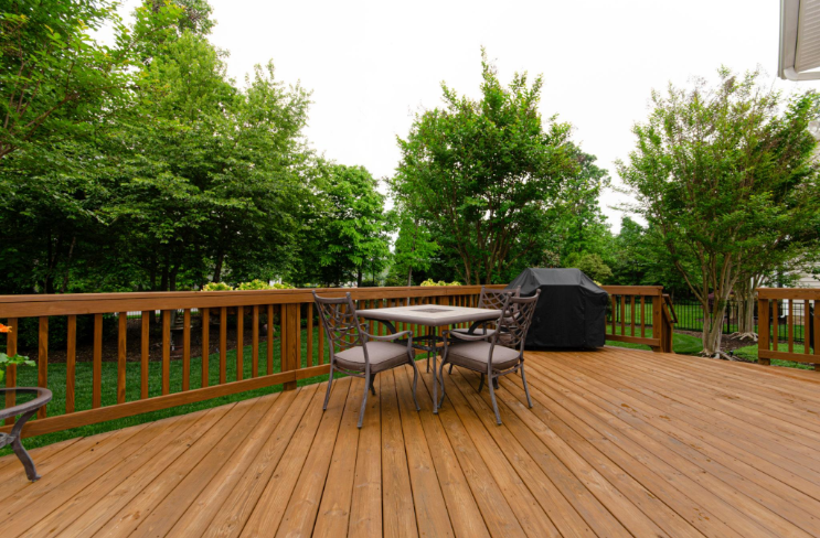“Spacious wood deck with railing, outdoor table, grill, and green backyard views by deck builders in Hampton, VA”