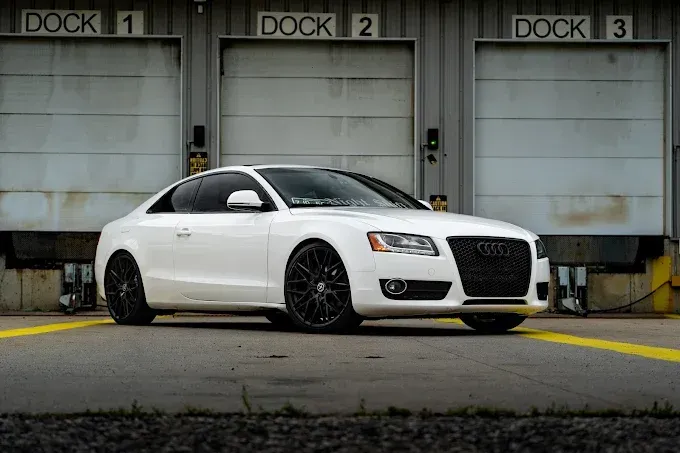 A white audi a5 coupe is parked in front of a dock.