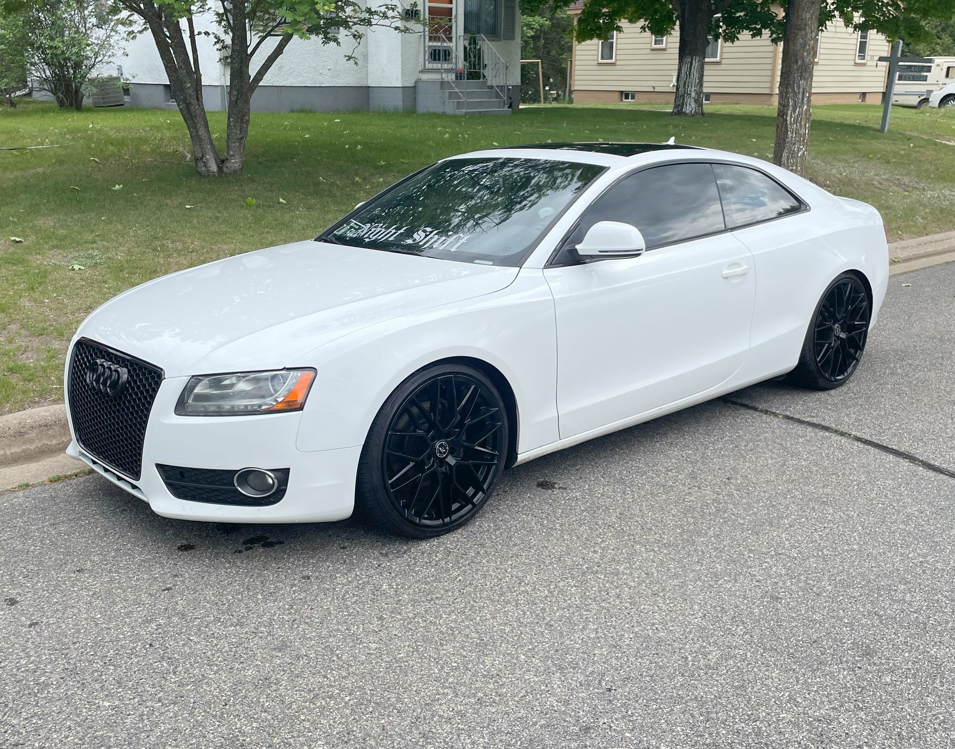 A white audi a5 coupe is parked on the side of the road.