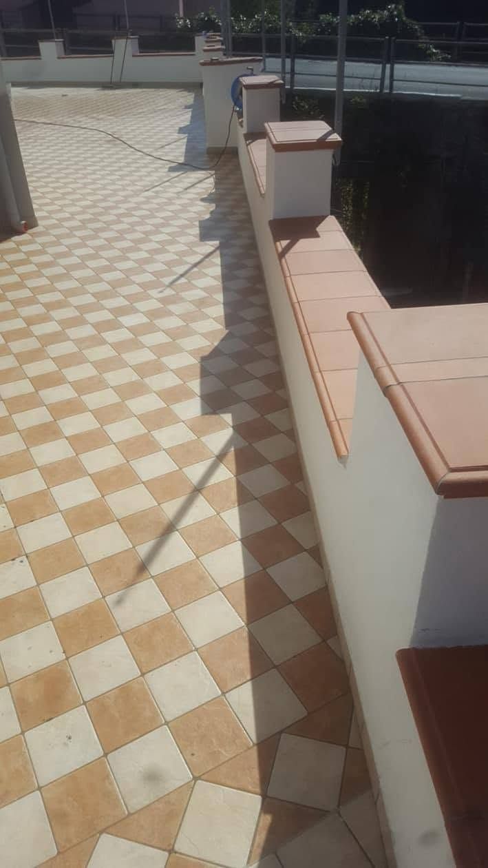 Passerella sul tetto piastrellata con muretto e ringhiera lungo il bordo, realizzata con piastrelle a scacchiera beige e bianche.