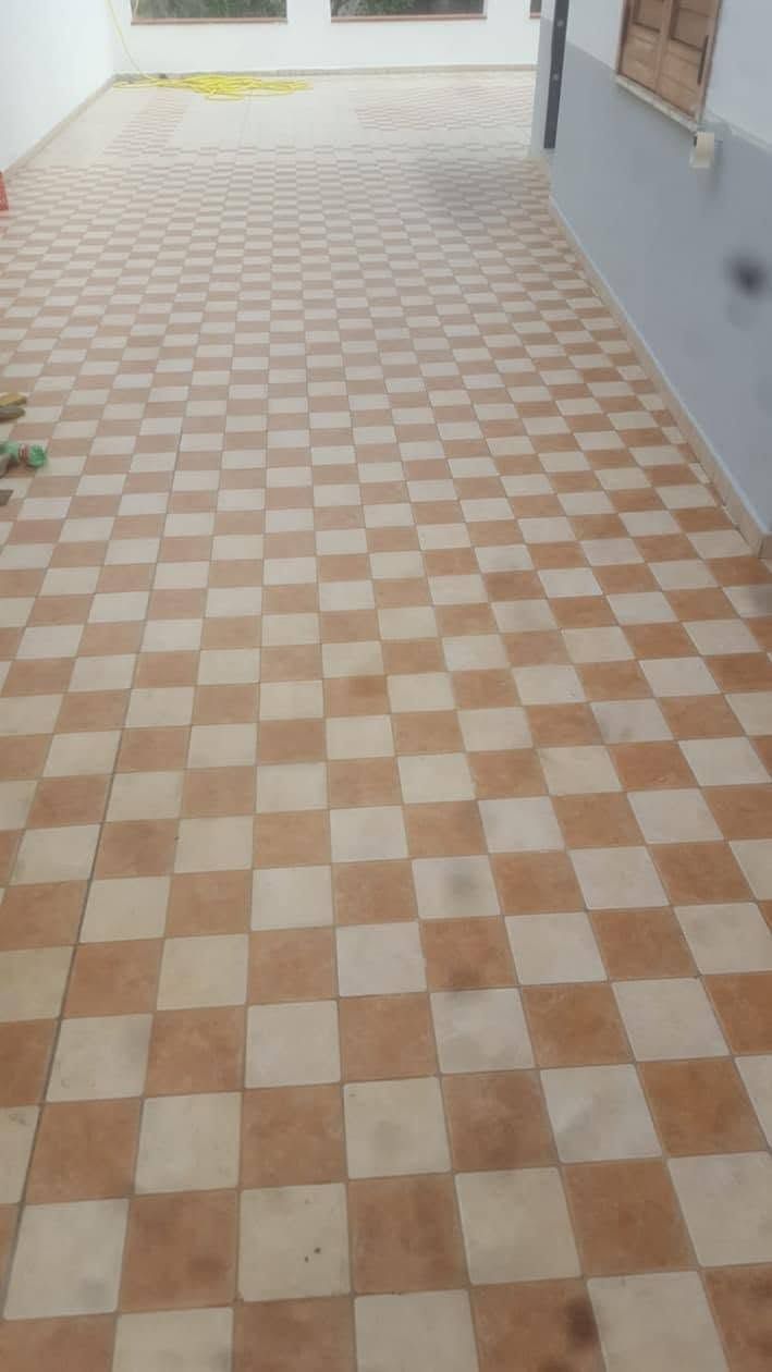 Corridoio con pavimento a scacchiera, pareti bianche e una luminosa apertura in fondo.