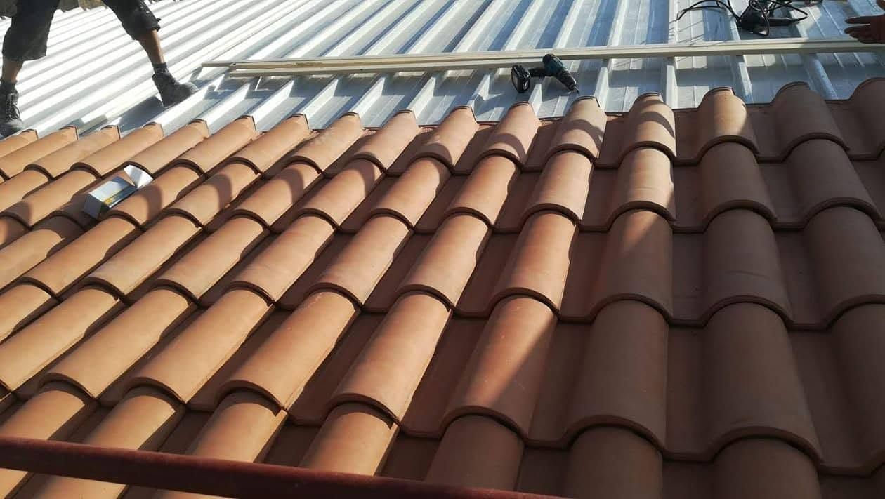 In primo piano, file di tegole di terracotta, con una copertura in lamiera ondulata sullo sfondo.
