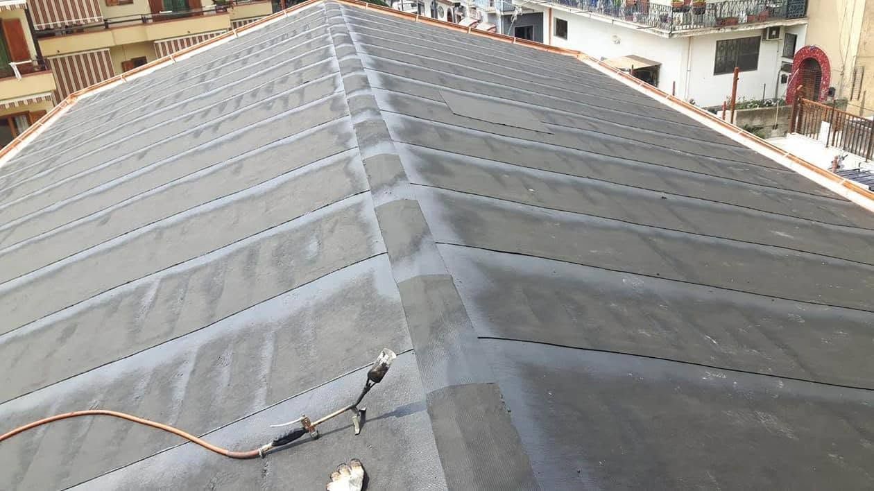 Tetto con pannelli metallici grigi a giunzione verticale e colmo centrale, visto dall'alto.