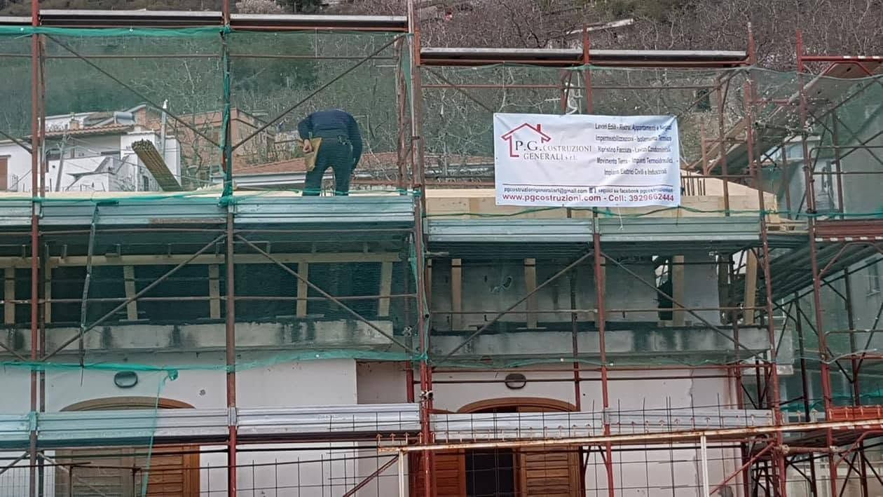 Operaio su un'impalcatura in un cantiere edile, accanto a uno striscione bianco.