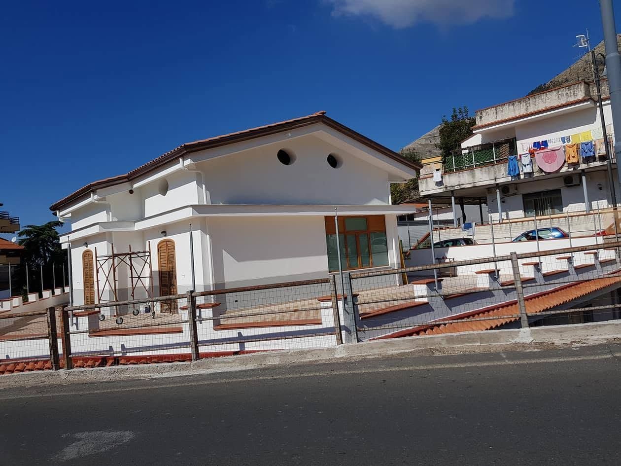 Edificio bianco sul lungomare con rampa e ringhiere a lato della strada sotto un cielo azzurro