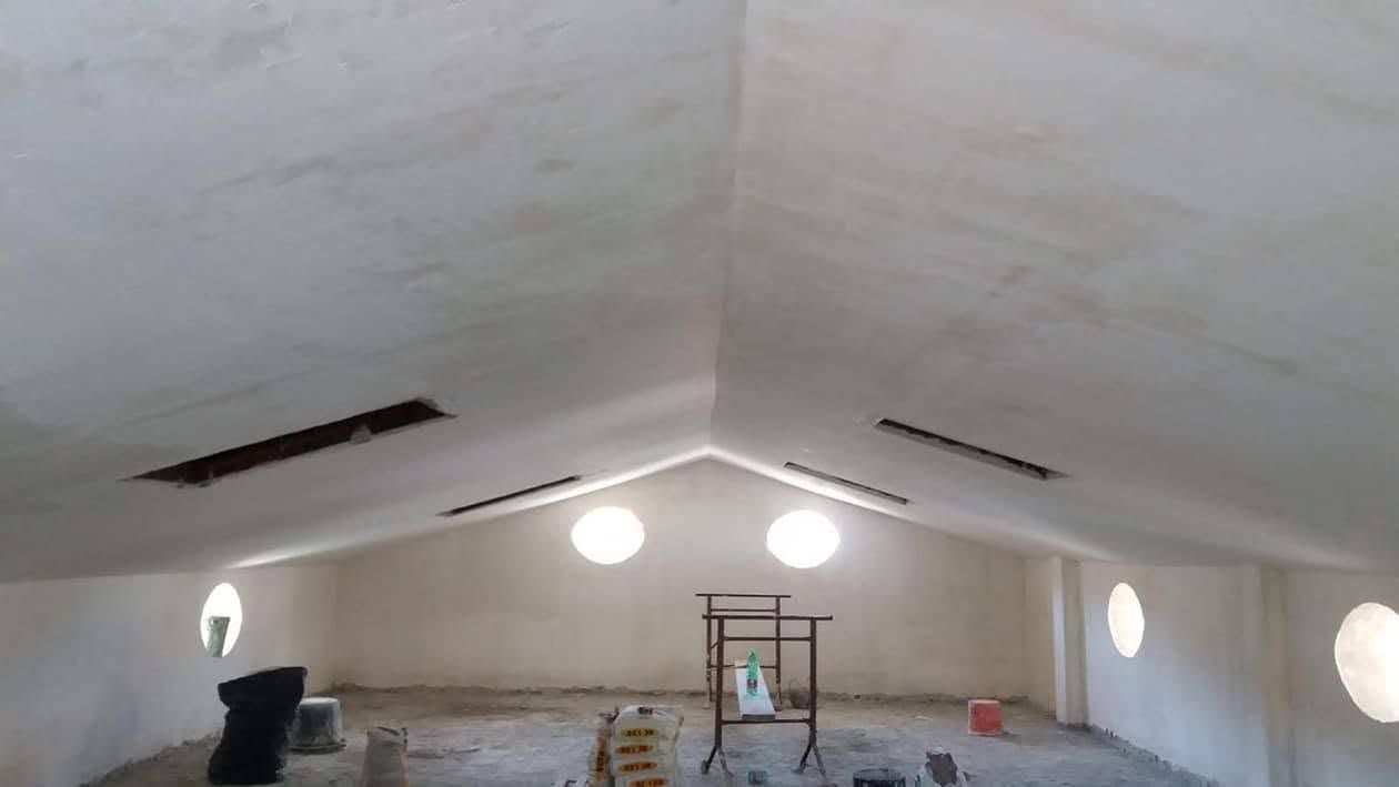 Mansarda in fase di ristrutturazione con pareti bianche, finestre rotonde e materiali edili sparsi ovunque.