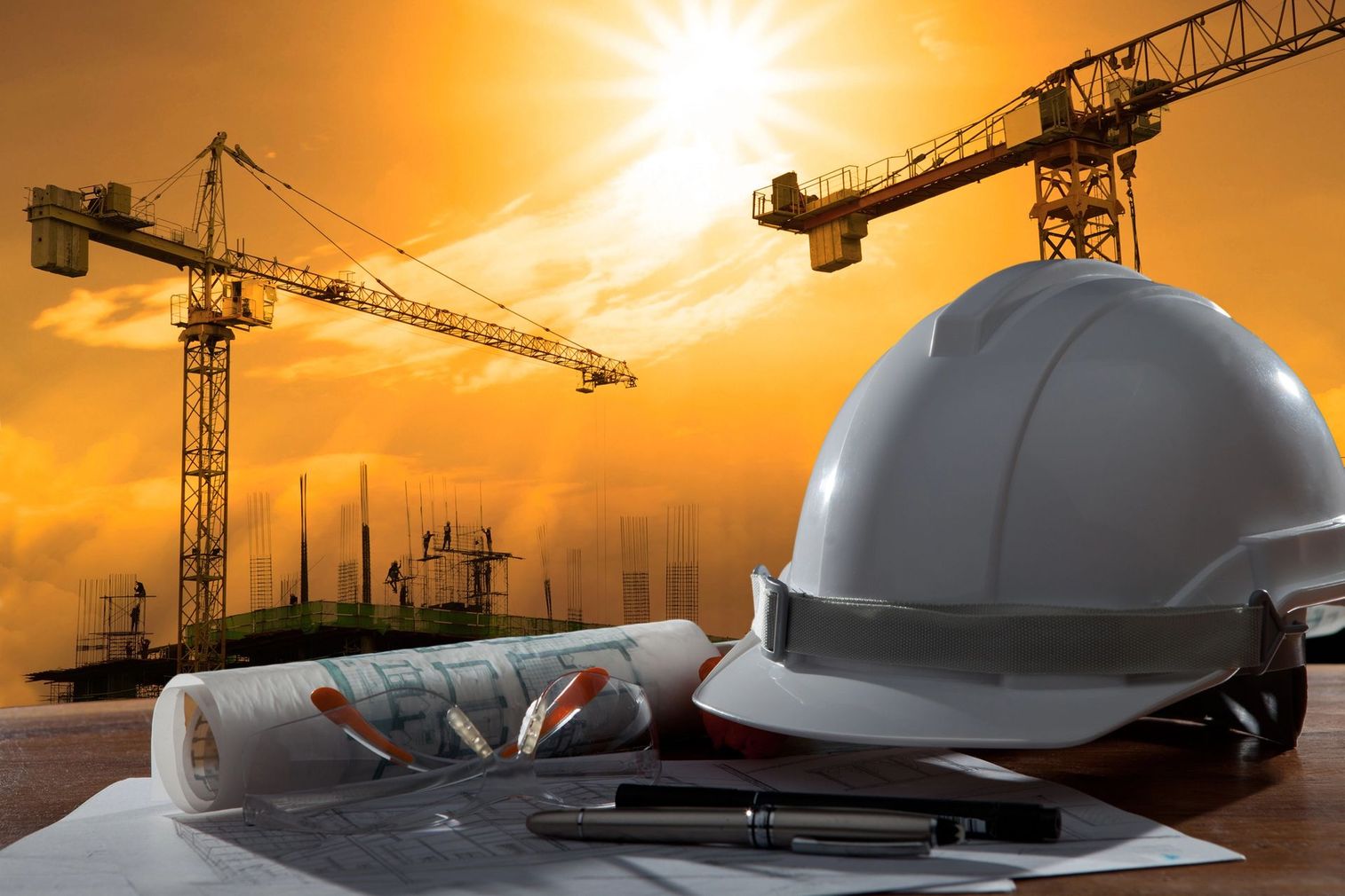Cantiere edile con gru, elmetto, progetto e un cielo luminoso all'alba.