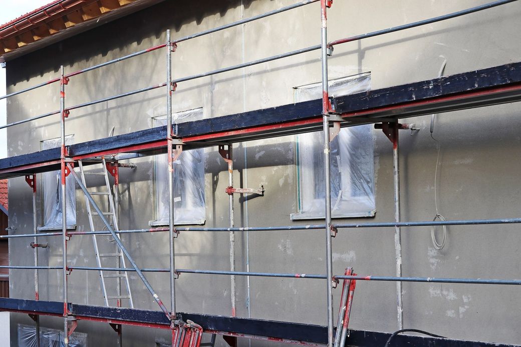 Facciata dell'edificio avvolta da impalcature e teli di plastica durante i lavori di ristrutturazione esterna.