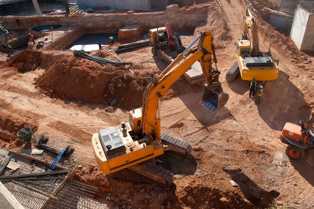 Escavatori e autocarro ribaltabile in un cantiere attivo con cumuli di terra e trincee.