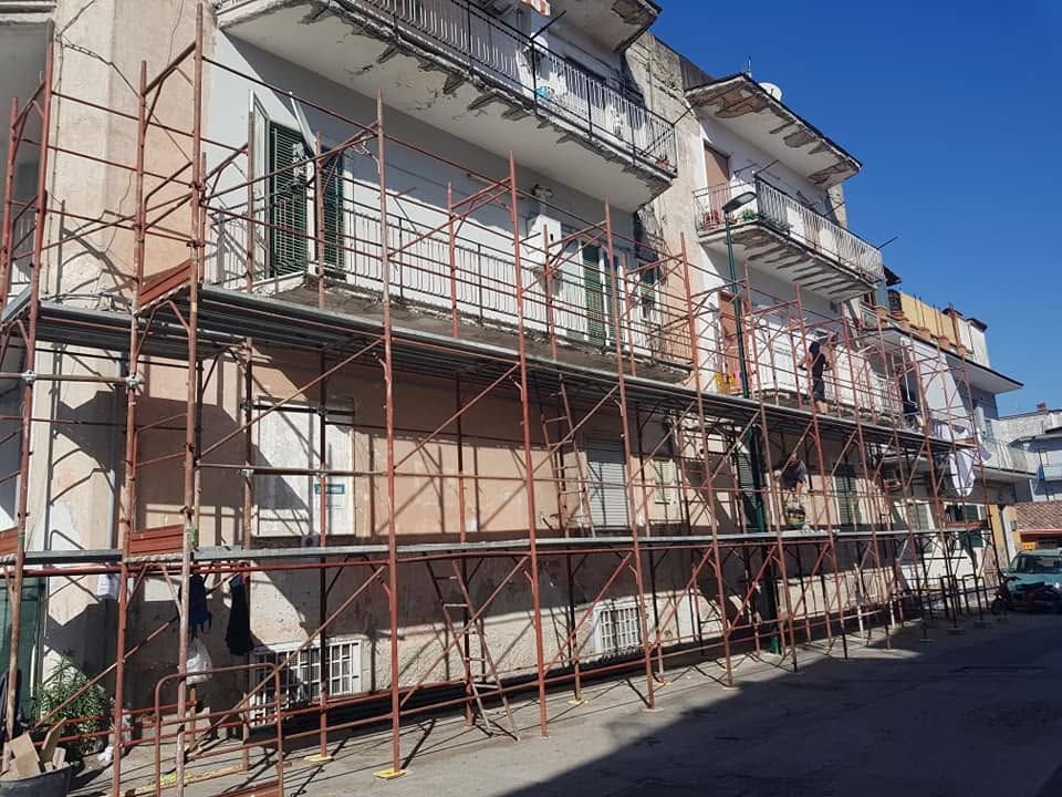 In una strada soleggiata, una fila di edifici è ricoperta da impalcature, a causa dei lavori di costruzione in corso.