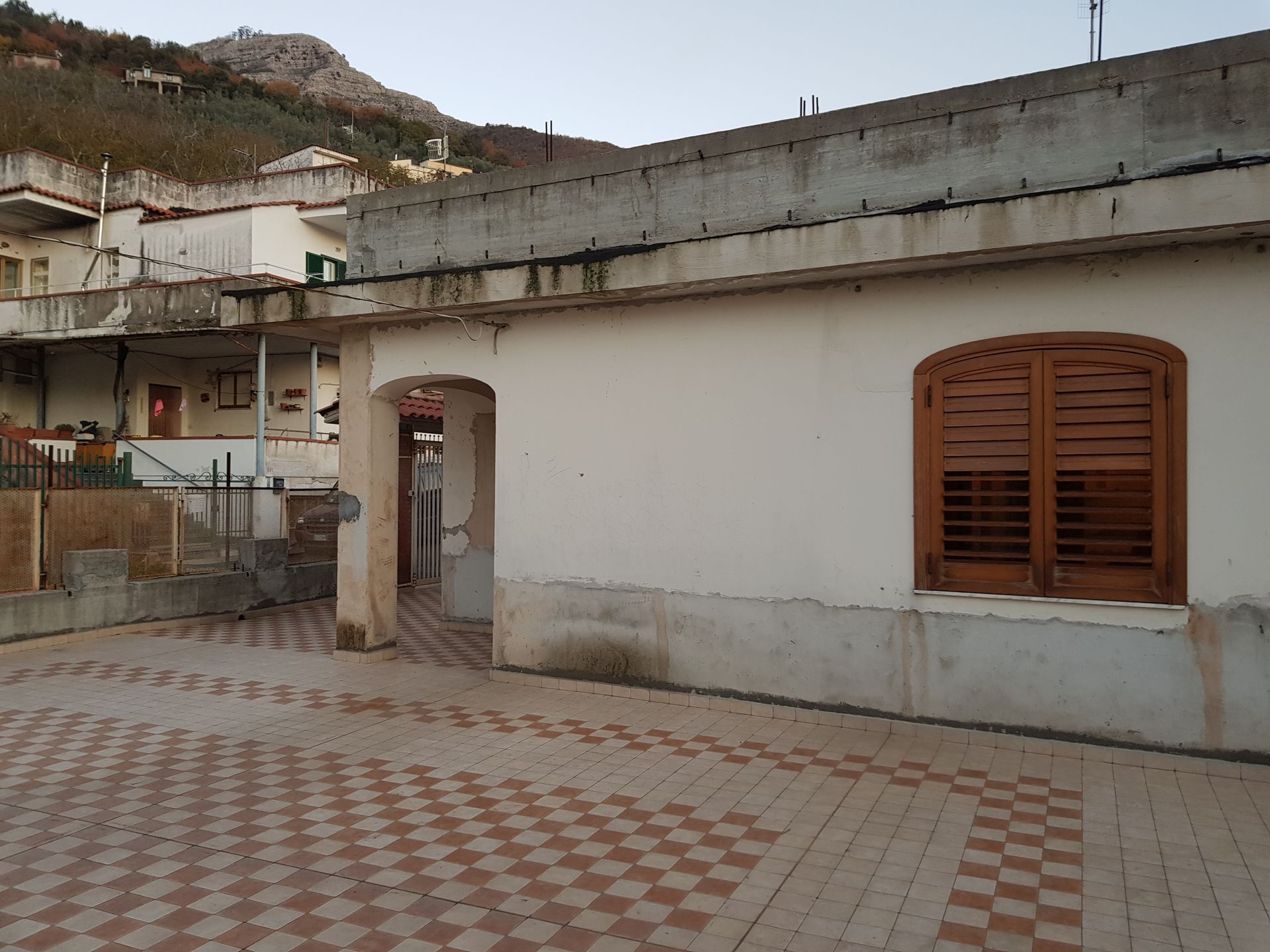 Una casa bianca con persiane marroni e un cortile piastrellato in un villaggio collinare.