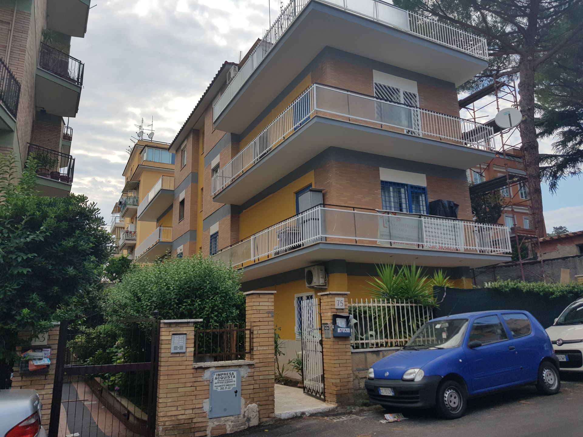 Condominio con balconi accanto a un'auto blu in una strada residenziale