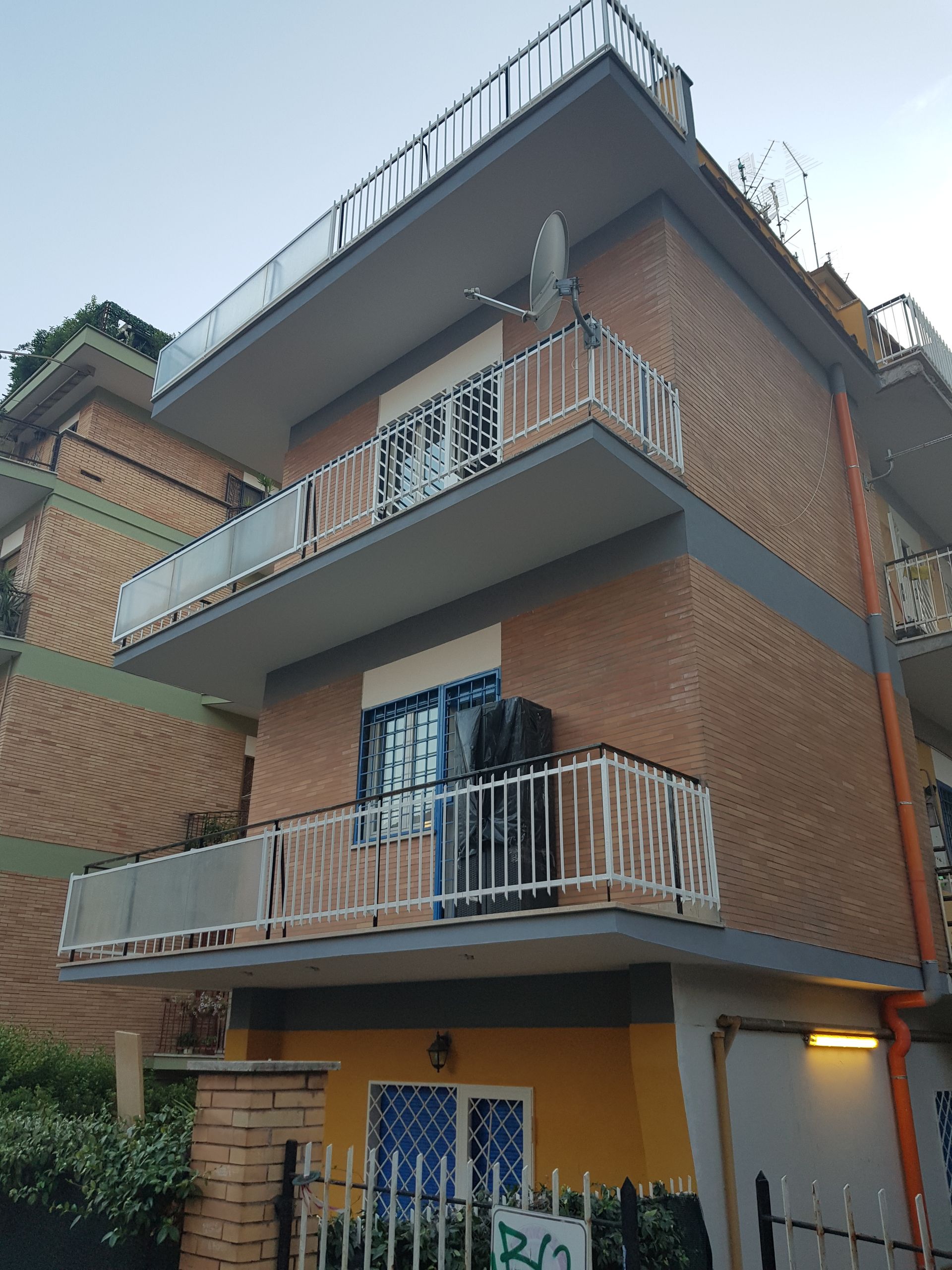 Casa a tre piani in mattoni con balconi grigi e porta blu sotto un cielo nuvoloso